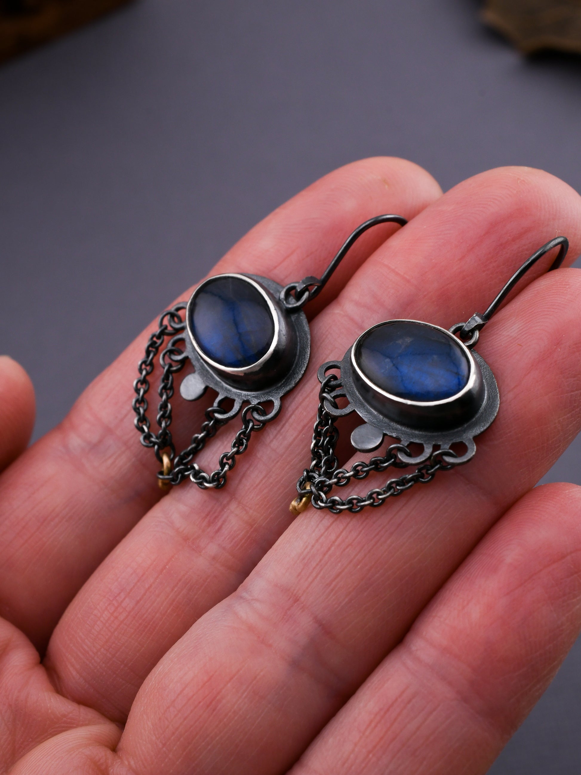 Pair of silver earrings with blue stones held in a hand against a dark background