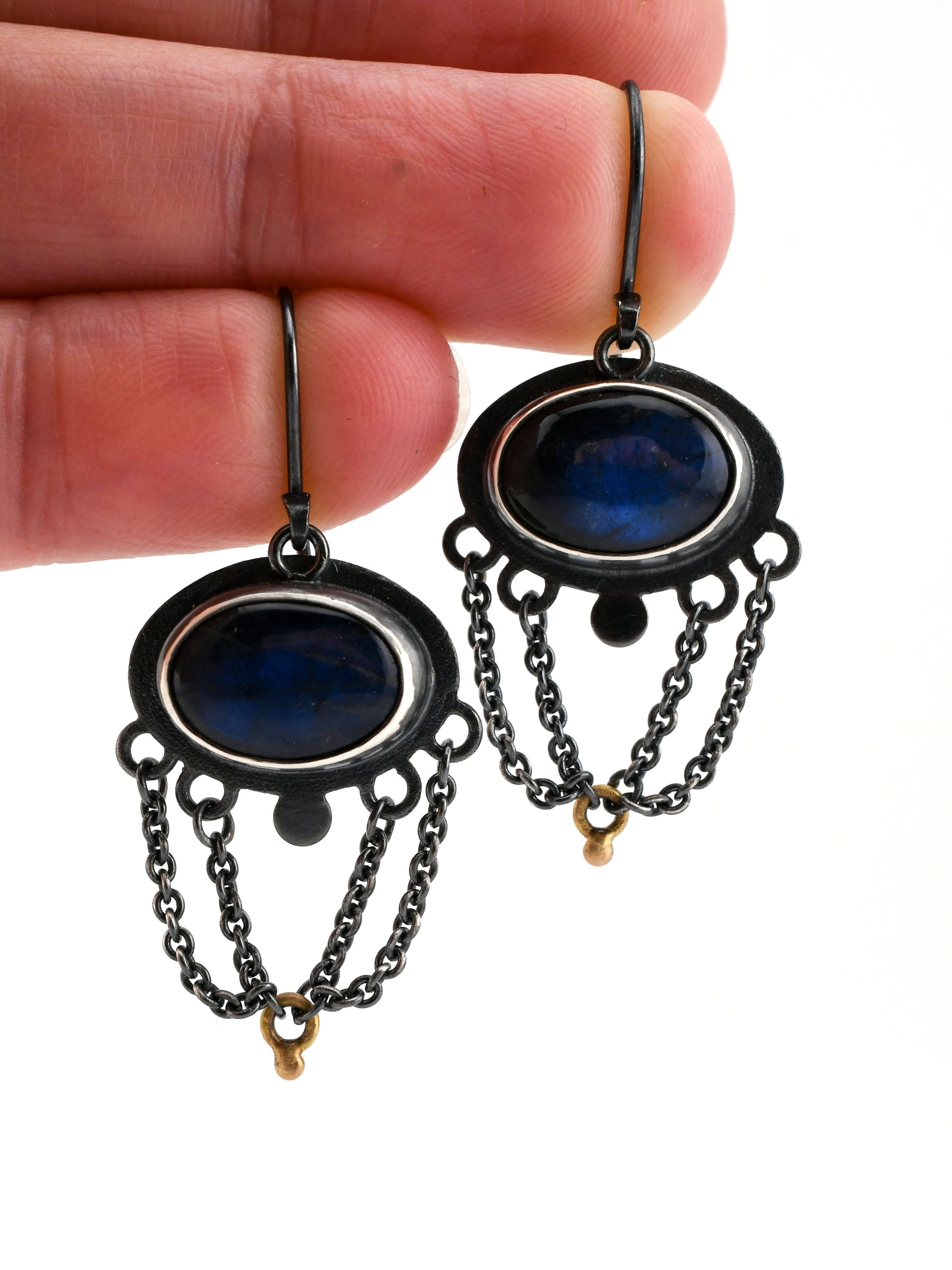 Black and gold earrings with blue stones held between fingers on a white background