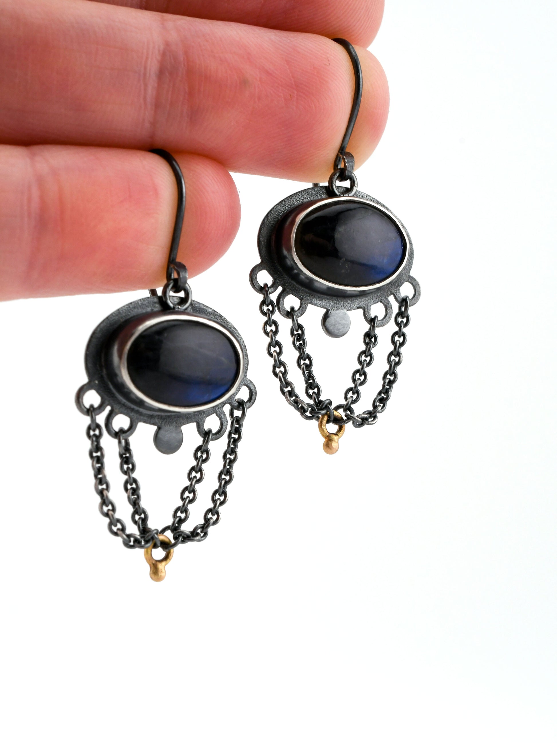 Black chain earrings with dark stones held between fingers on a white background