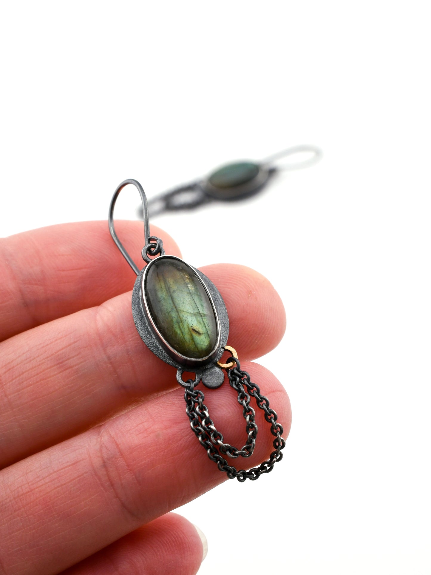 Jewelry with a green stone held between fingers on a white background