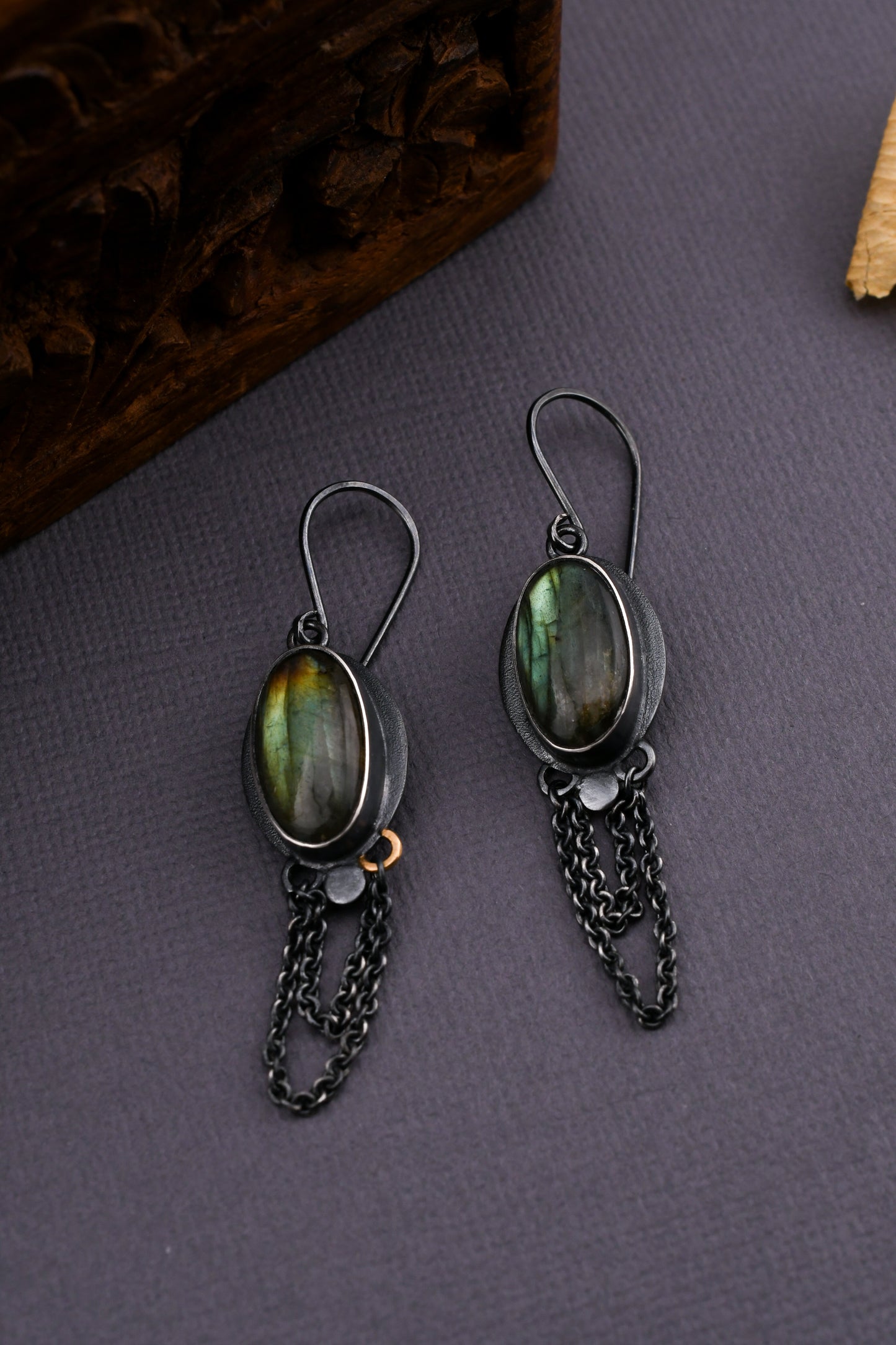 Pair of earrings with green gemstones and chain details on a gray surface.