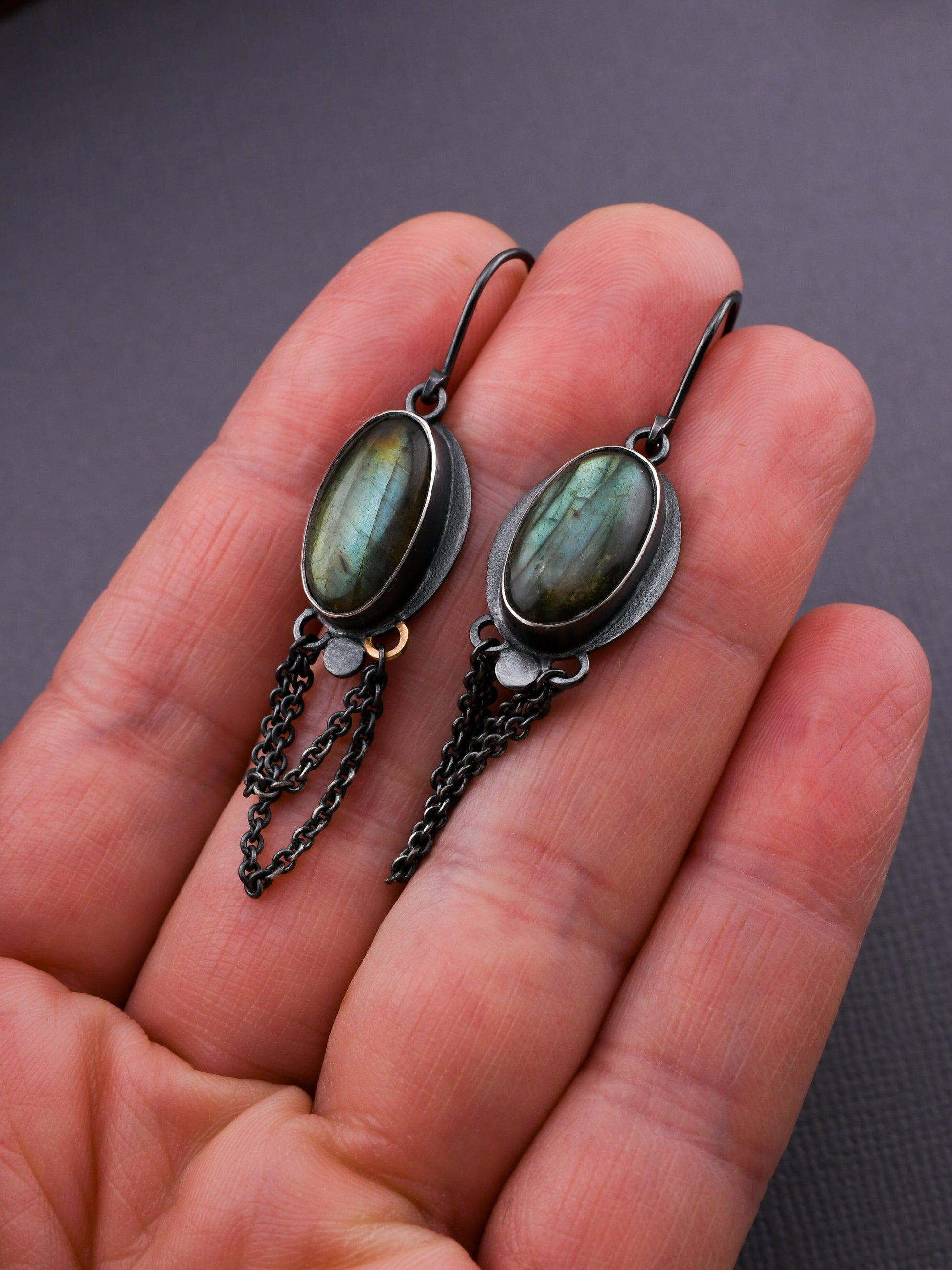 Earrings with green stones and chains held in a hand against a dark background