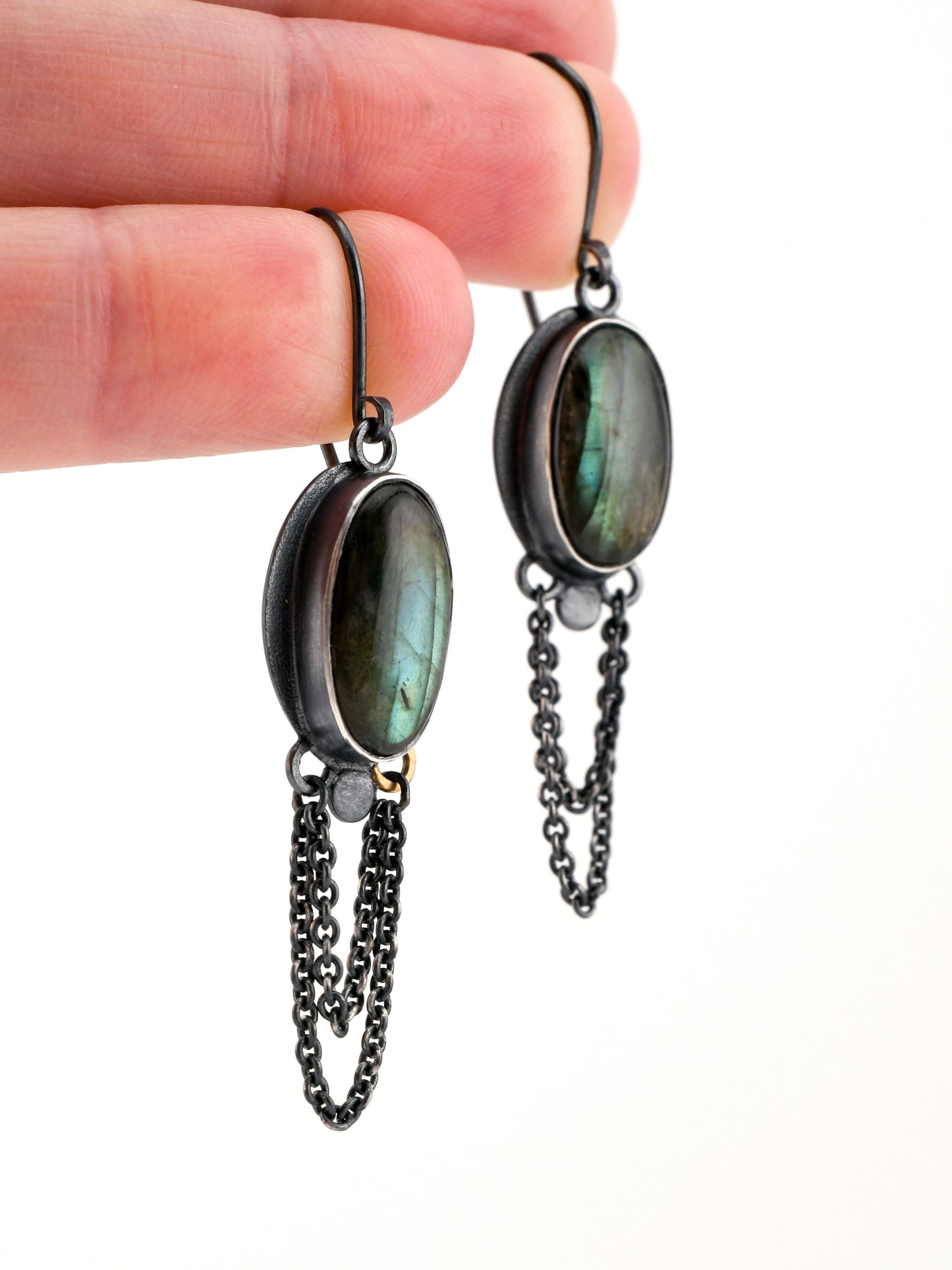 Labradorite earrings with chains held by a hand on a white background
