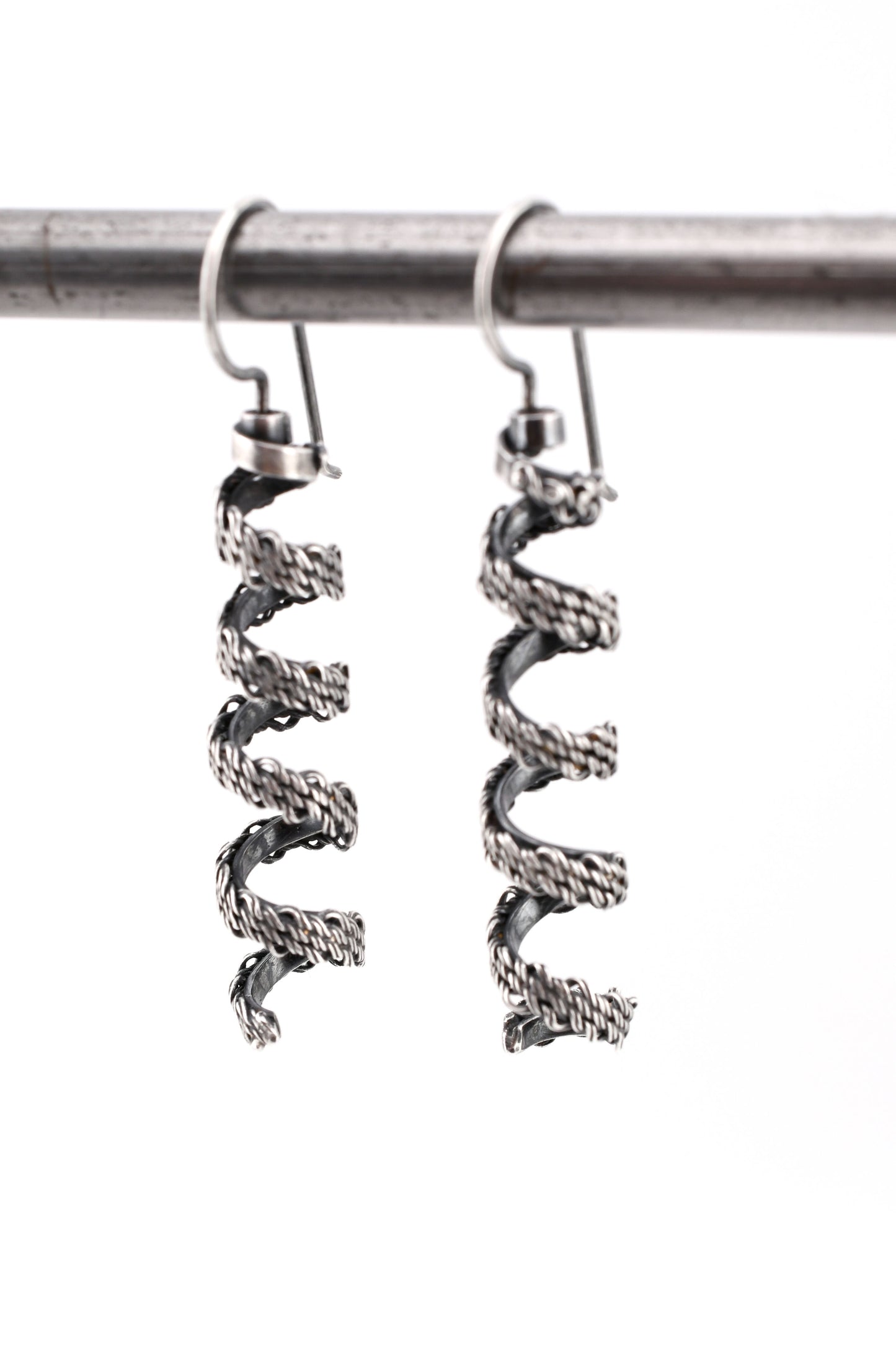 woven silver spiral earrings hanging over a white background