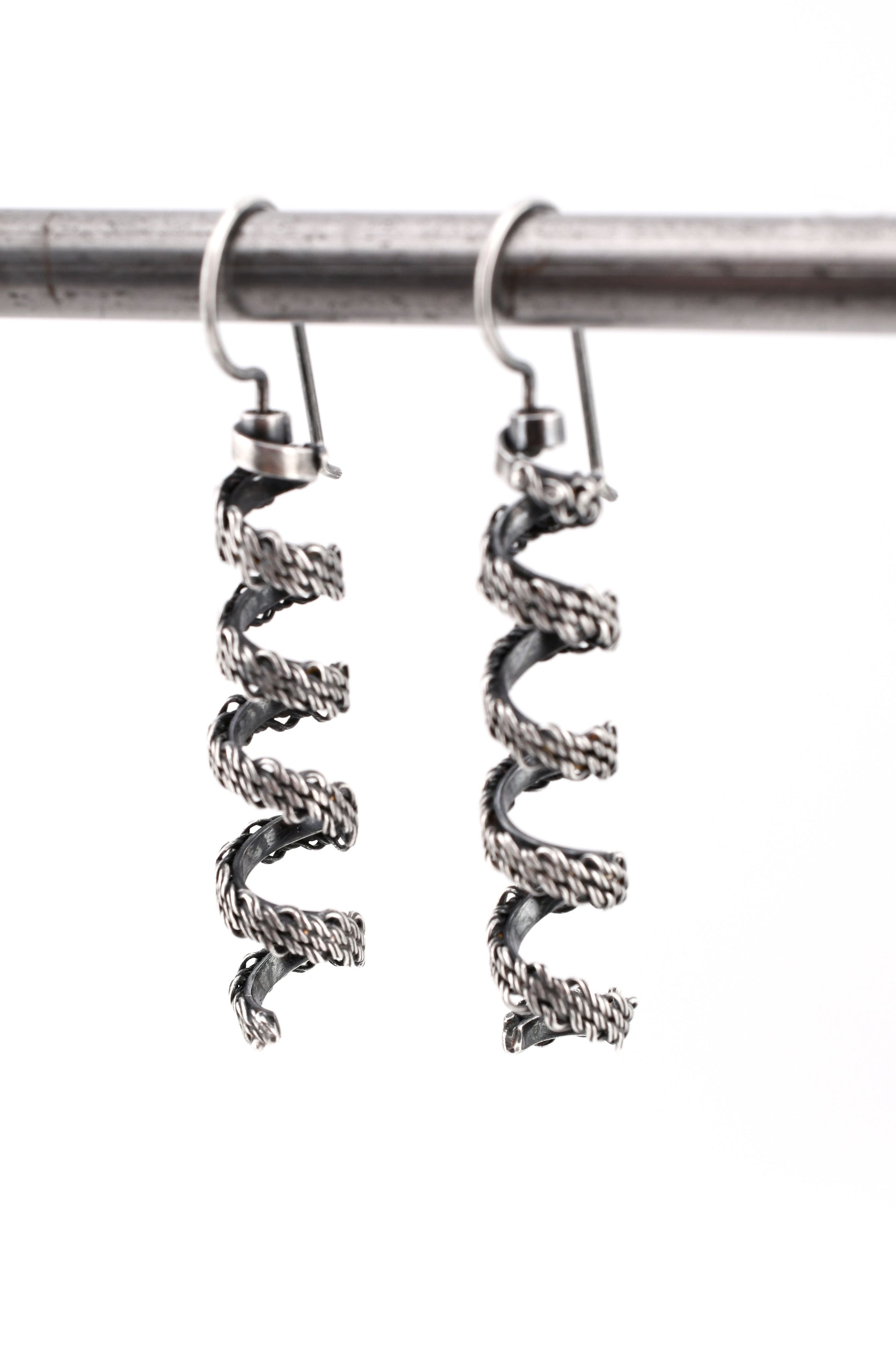 woven silver spiral earrings hanging over a white background