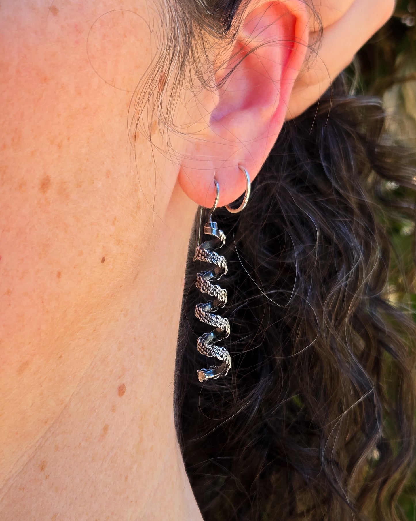 woven silver spiral earrings shown worn on an ear in natural light