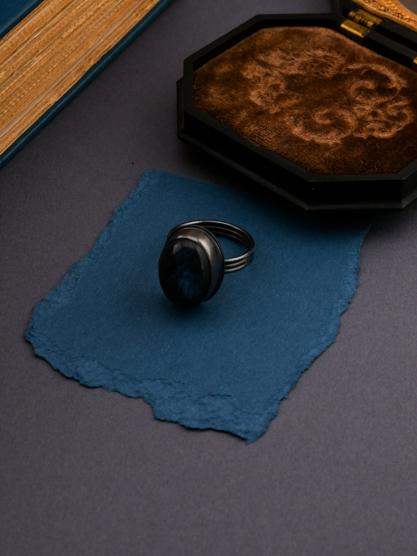 Black ring on a blue fabric with a textured box in the background