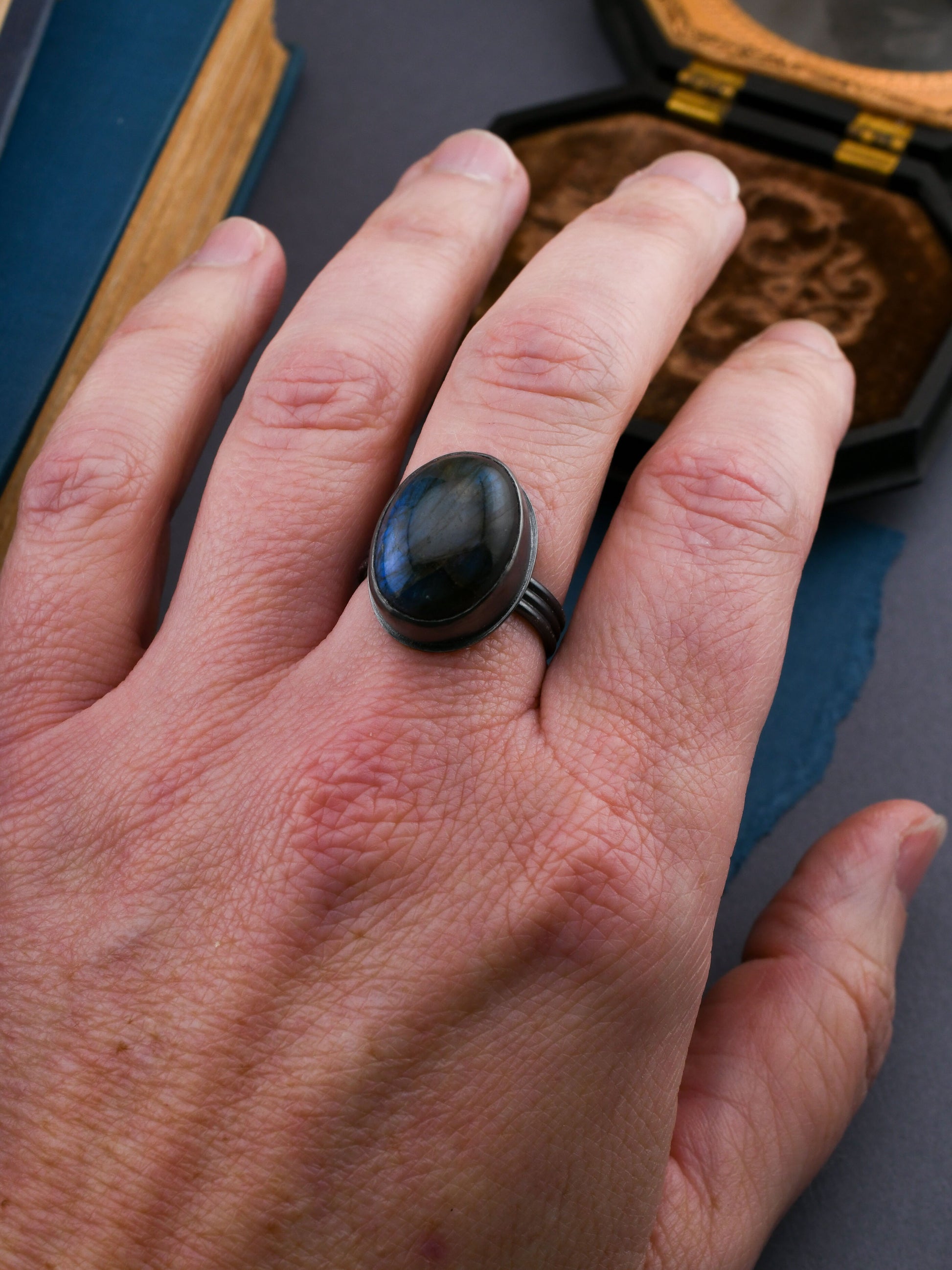 Hand wearing a black ring with a stone, set against a dark background