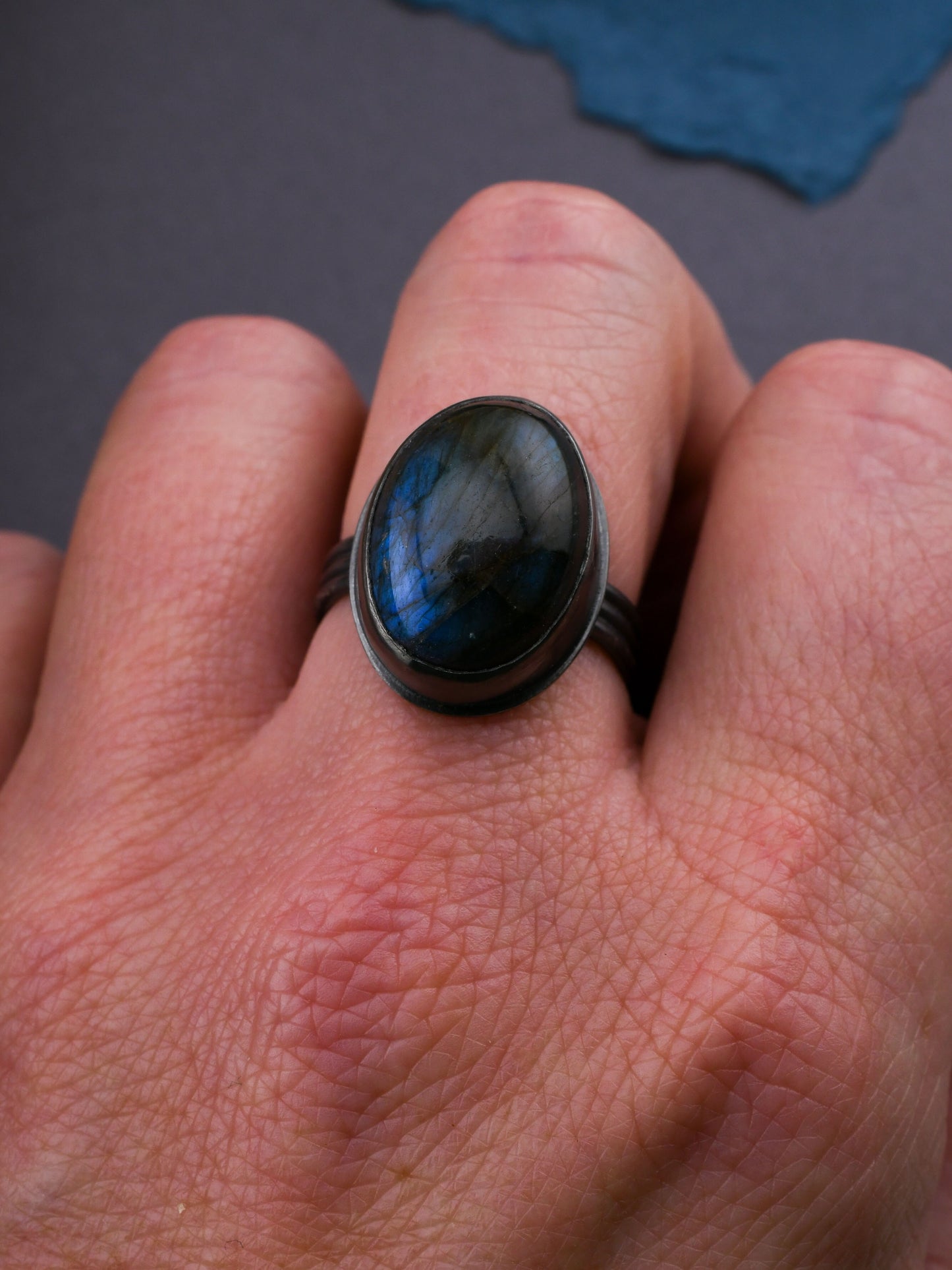 Close-up of a hand wearing a ring with a blue stone on a dark background