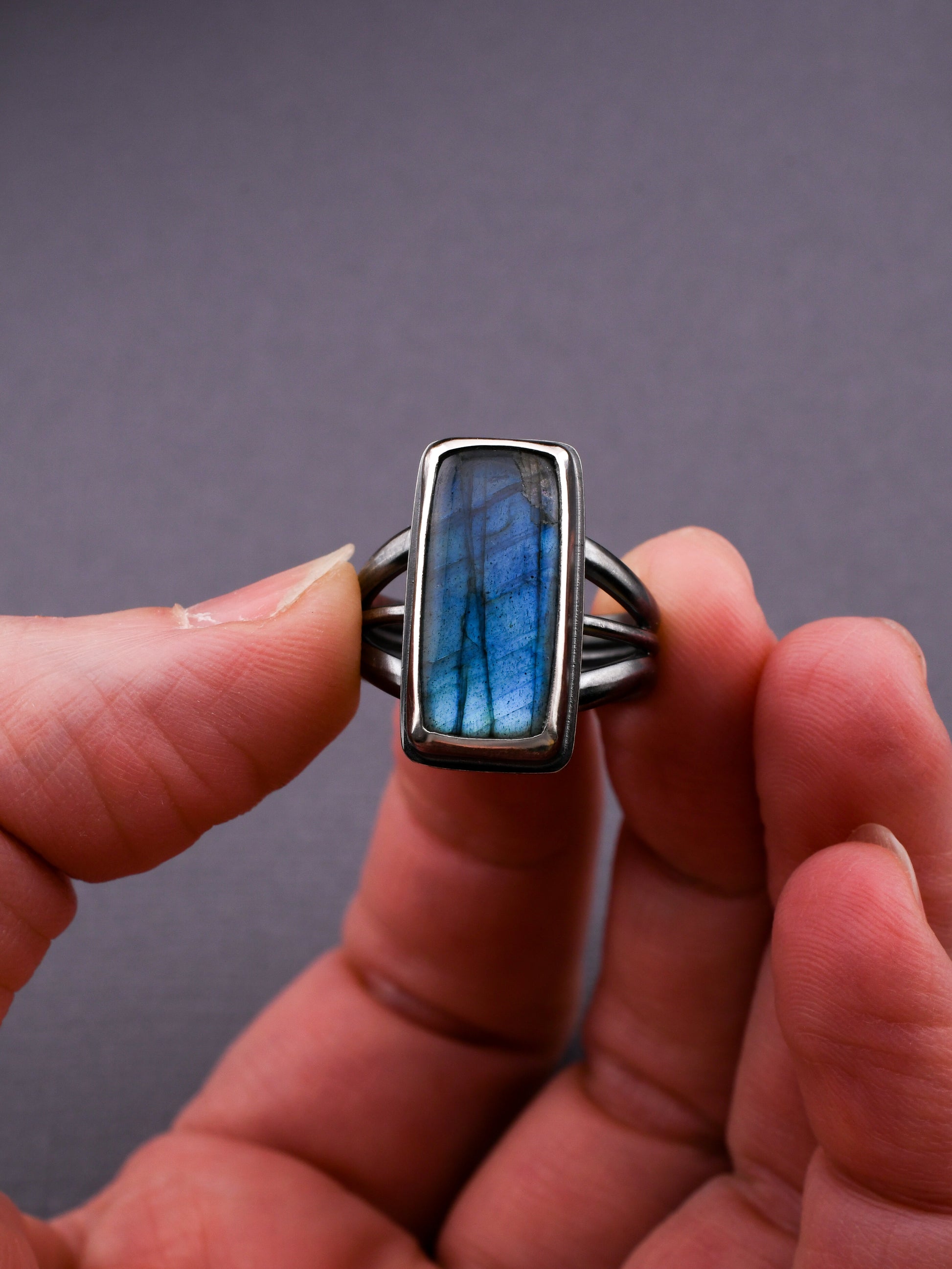 Ring with a blue stone held between fingers against a gray background
