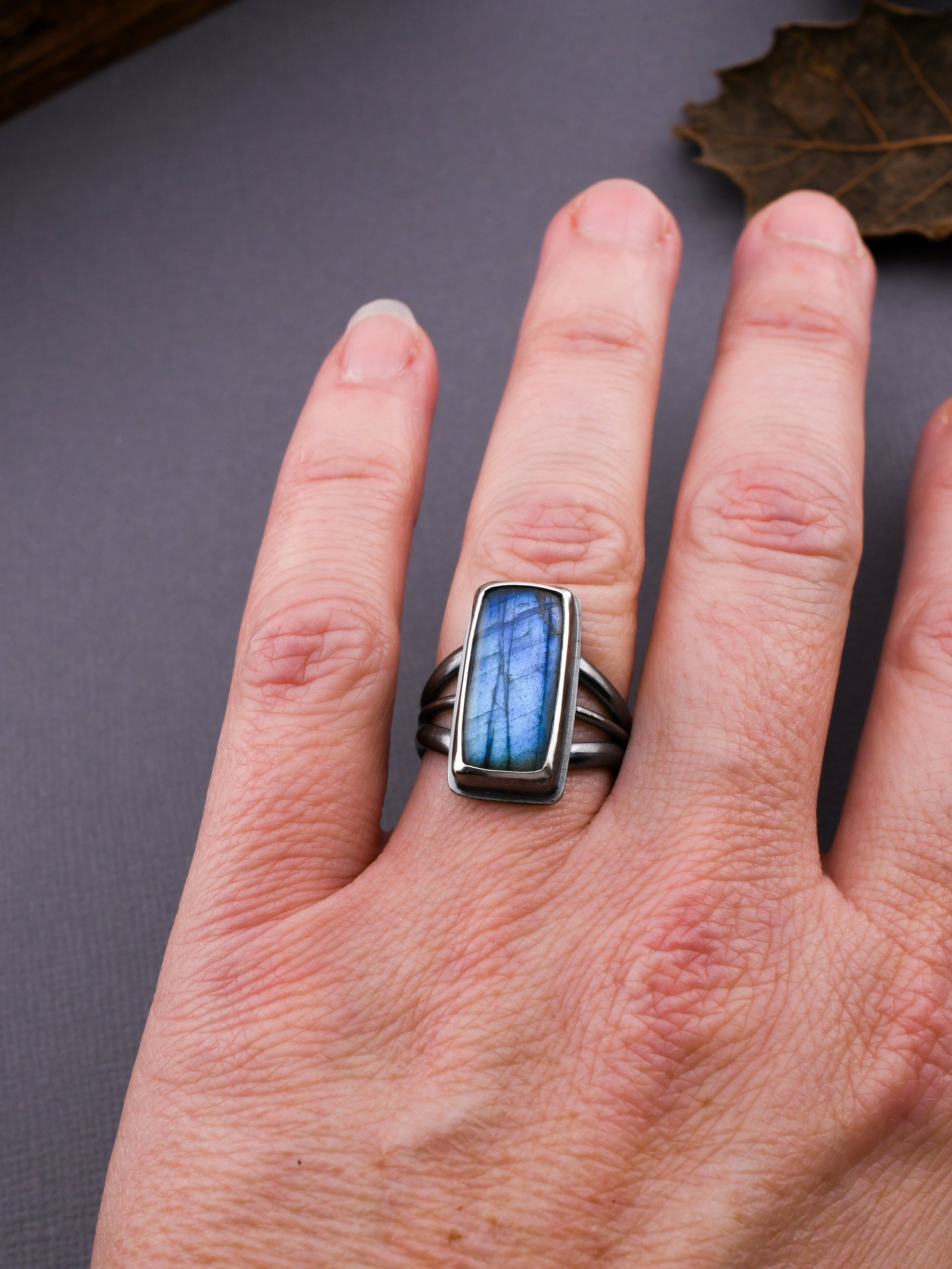 Hand wearing a silver ring with a blue stone on a gray background