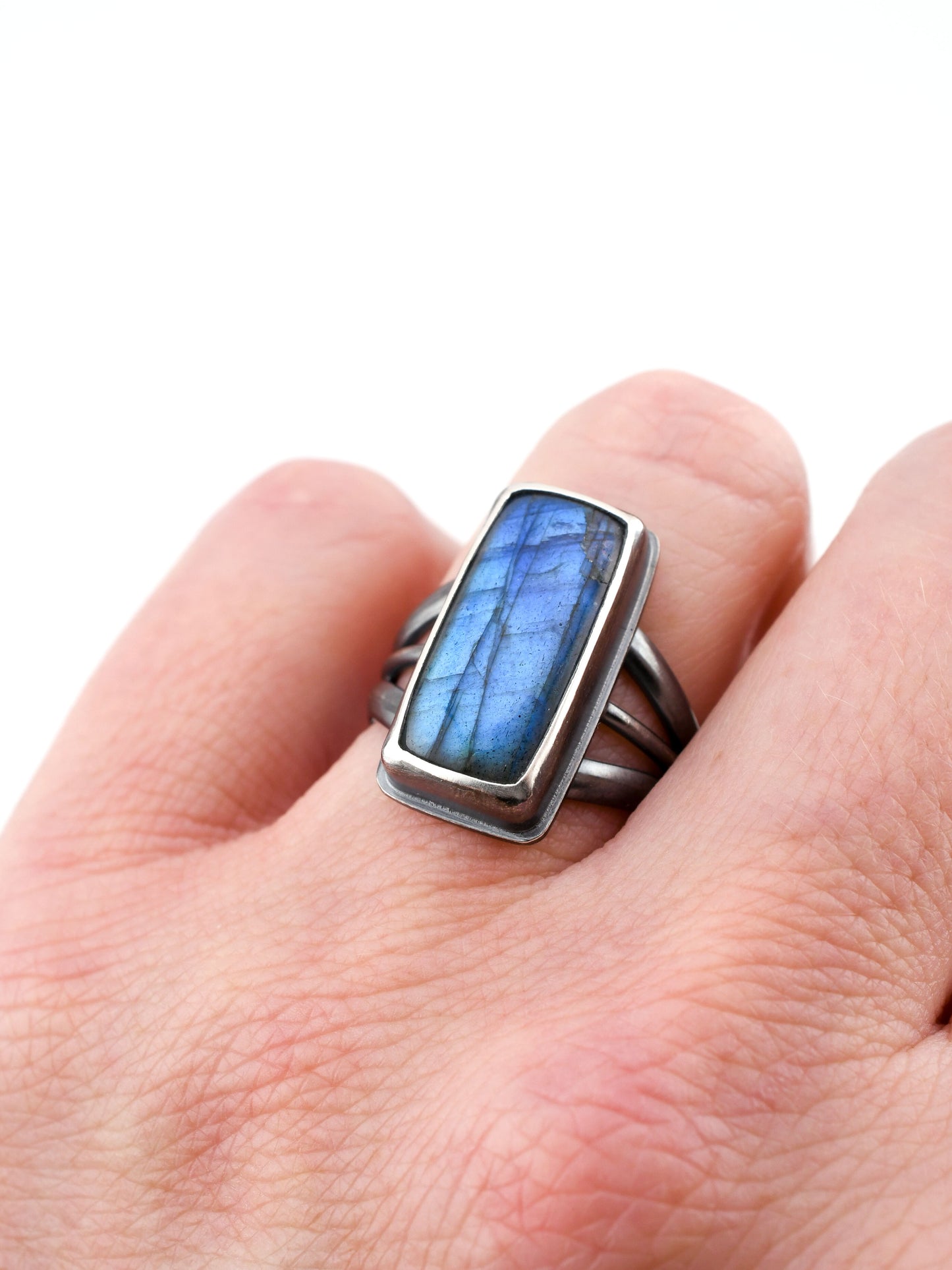 Silver ring with a blue stone on a hand against a white background