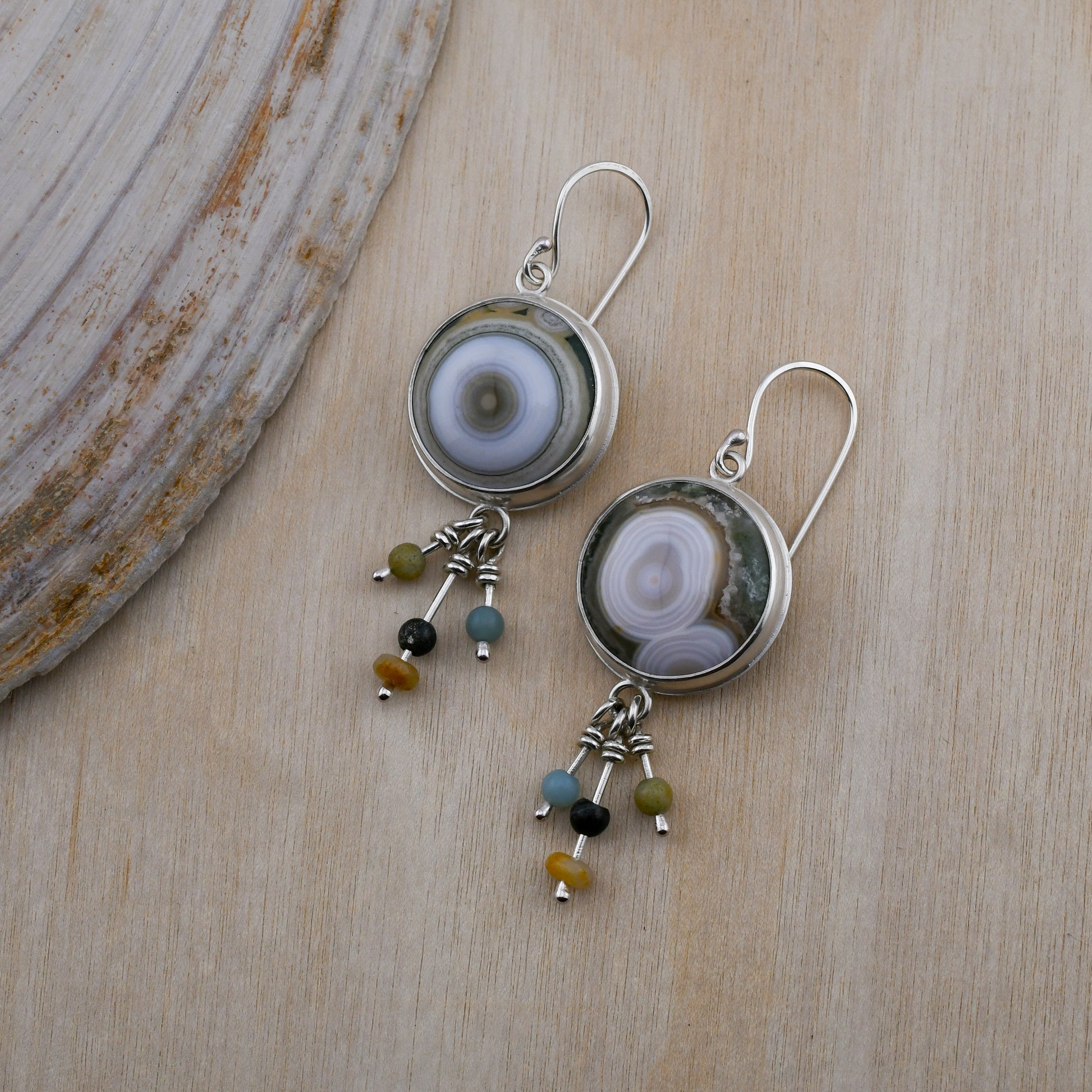 Silver earrings with circular ocean jasper stones and bead drops on a wooden surface