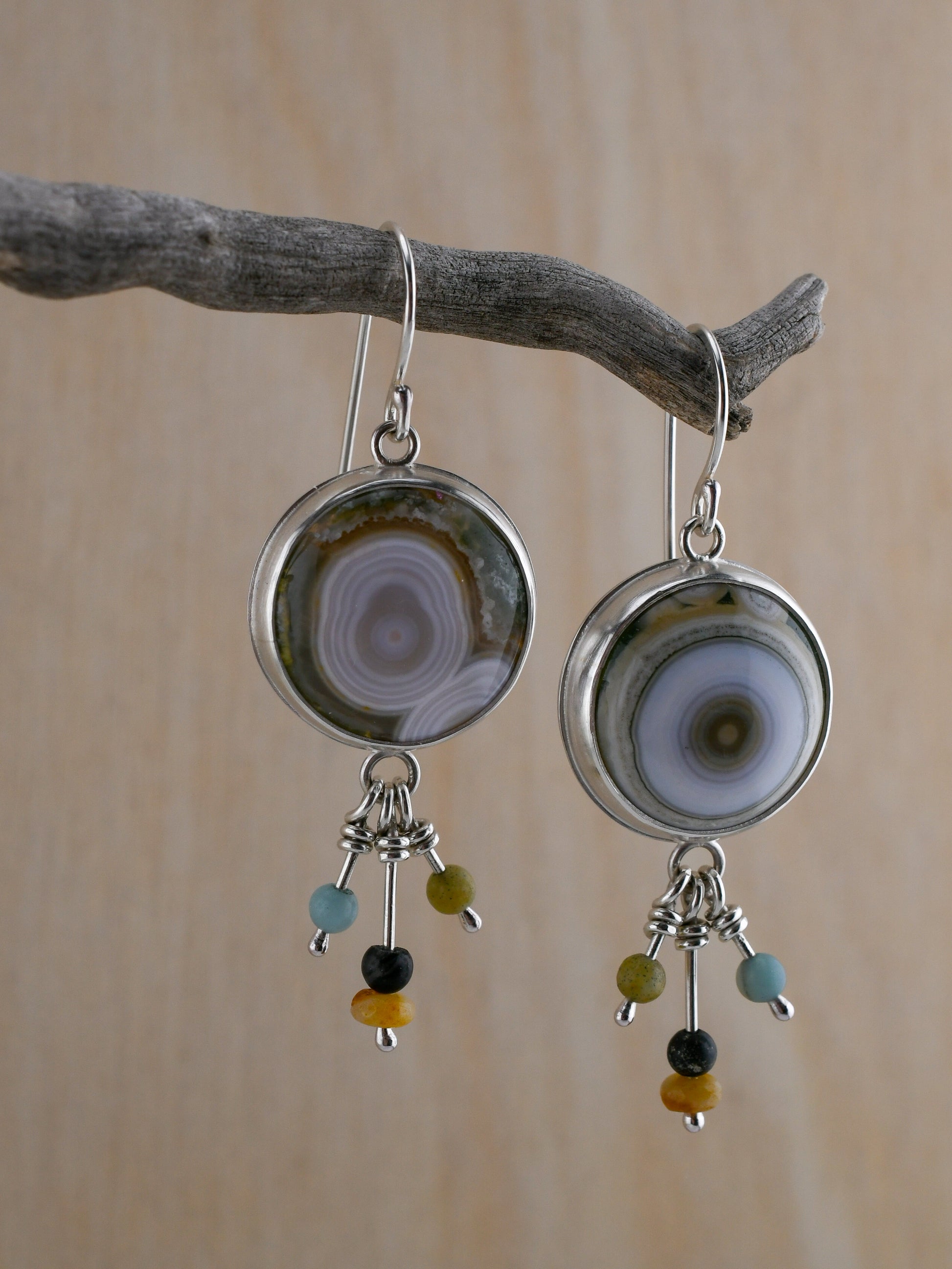 Silver earrings with round Ocean jaspers and beaded dangles hanging from a branch with a neutral background