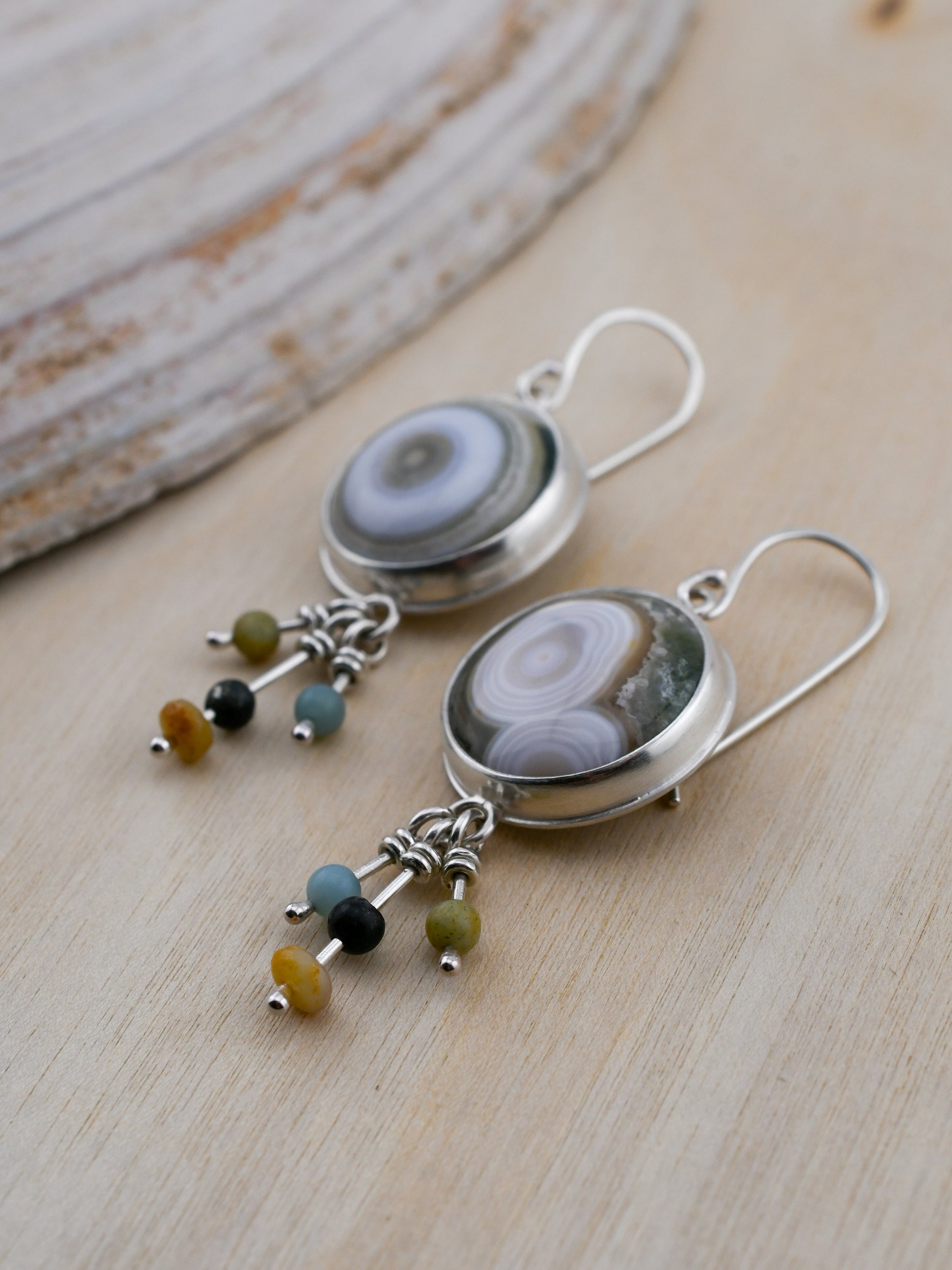 Pair of silver earrings with circular stone and bead charms on a wooden surface