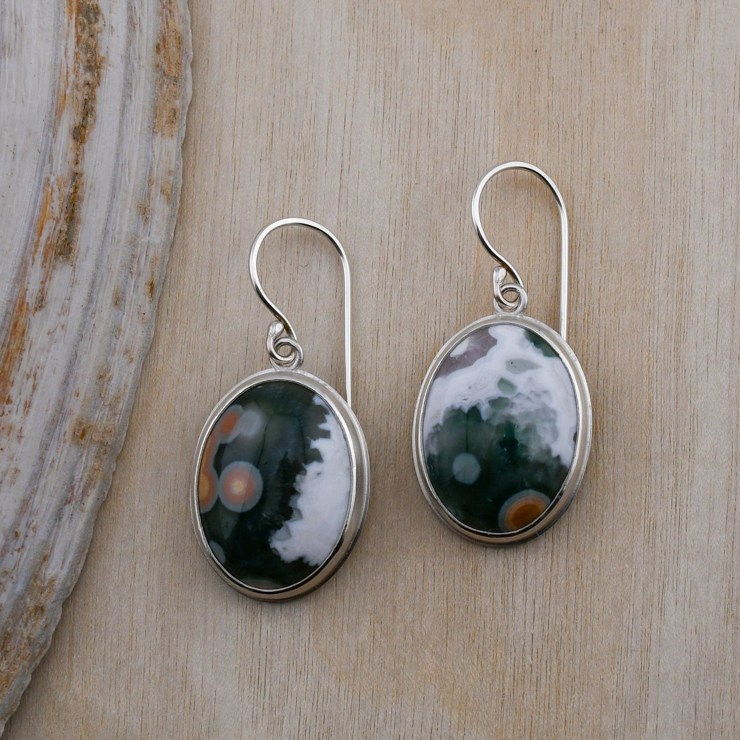 Pair of silver earrings with green and white stones on a wooden surface