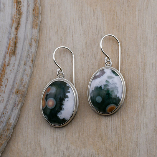 Pair of silver earrings with green and white stones on a wooden surface