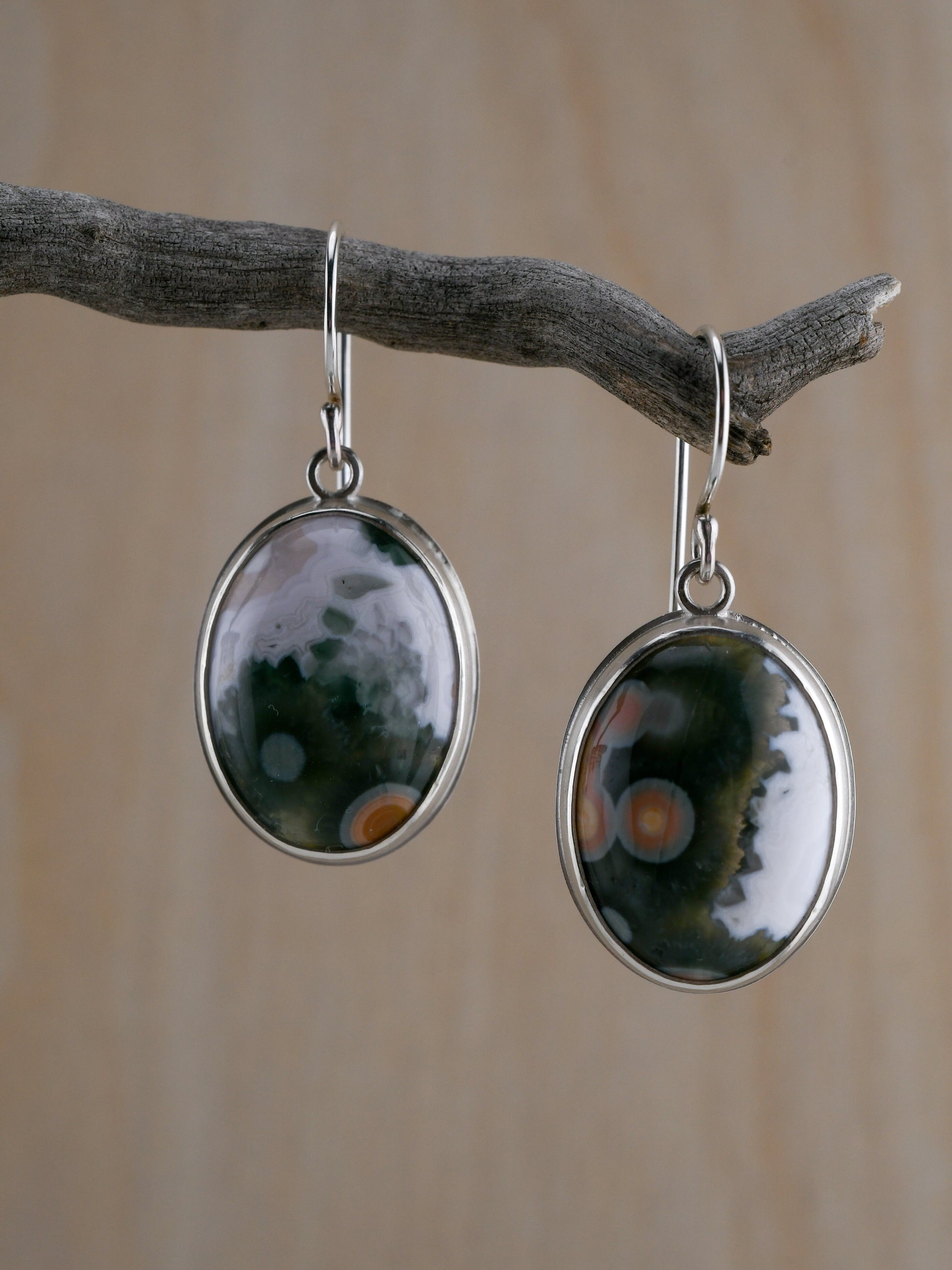 Pair of silver earrings with green, white and orange speckled stones hanging on a branch.