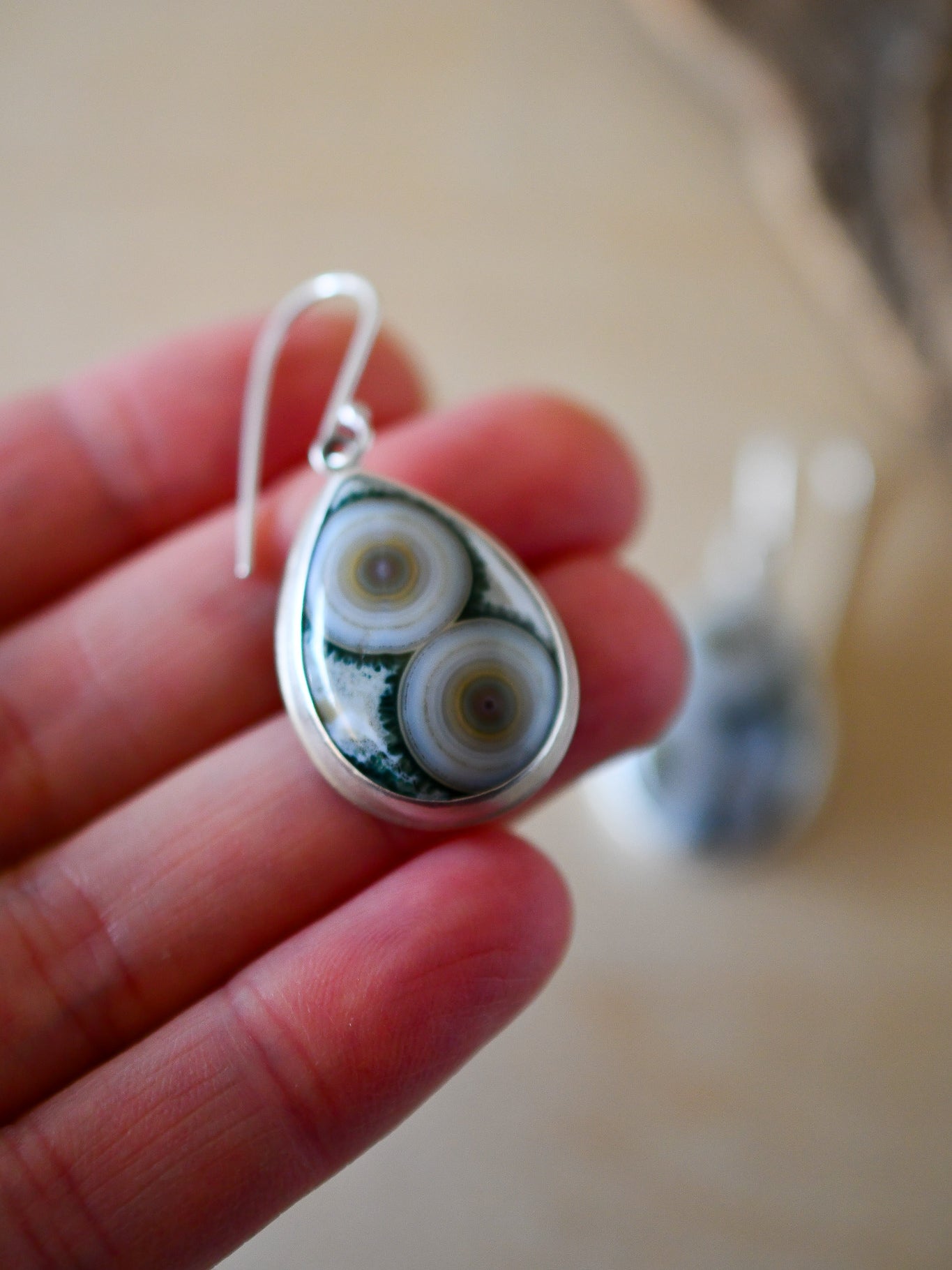 Teardrop-shaped earring with circular design held in a hand against a blurred background