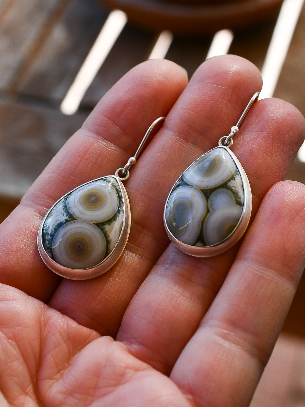 Teardrop-shaped earrings with intricate designs held in a hand.