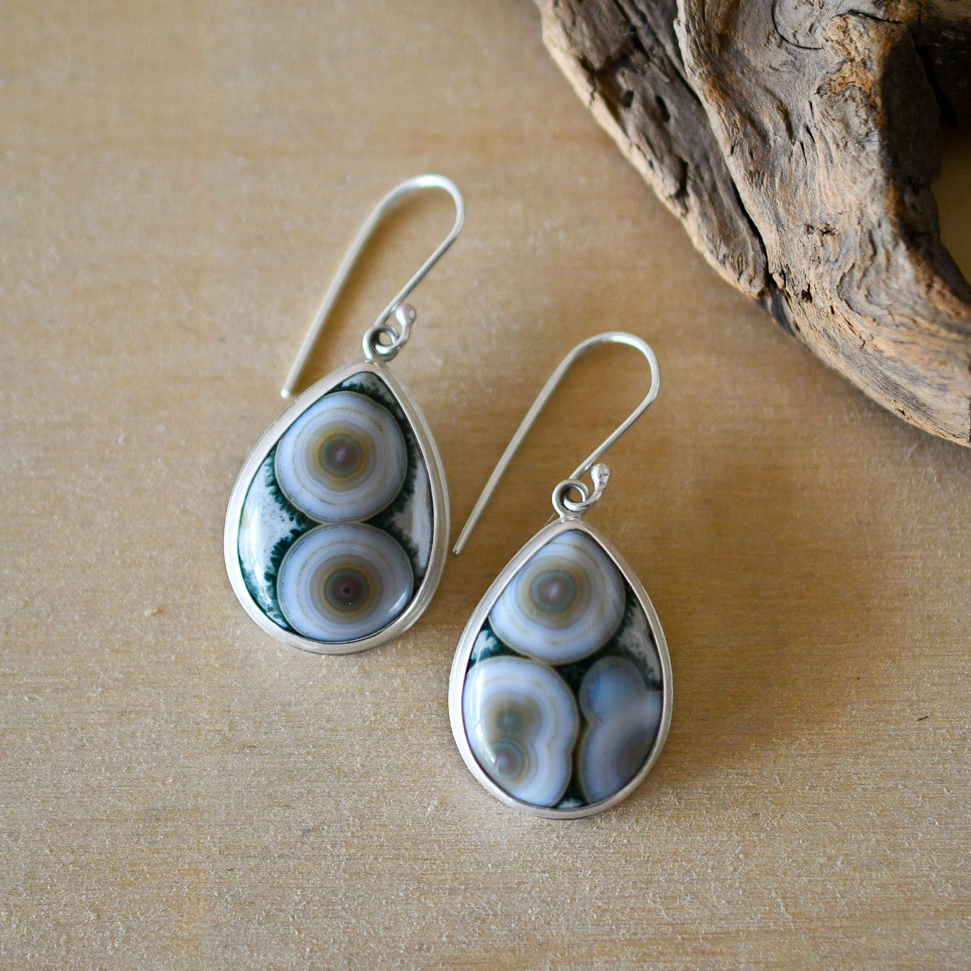 Teardrop-shaped earrings with a natural stone design on a wooden surface