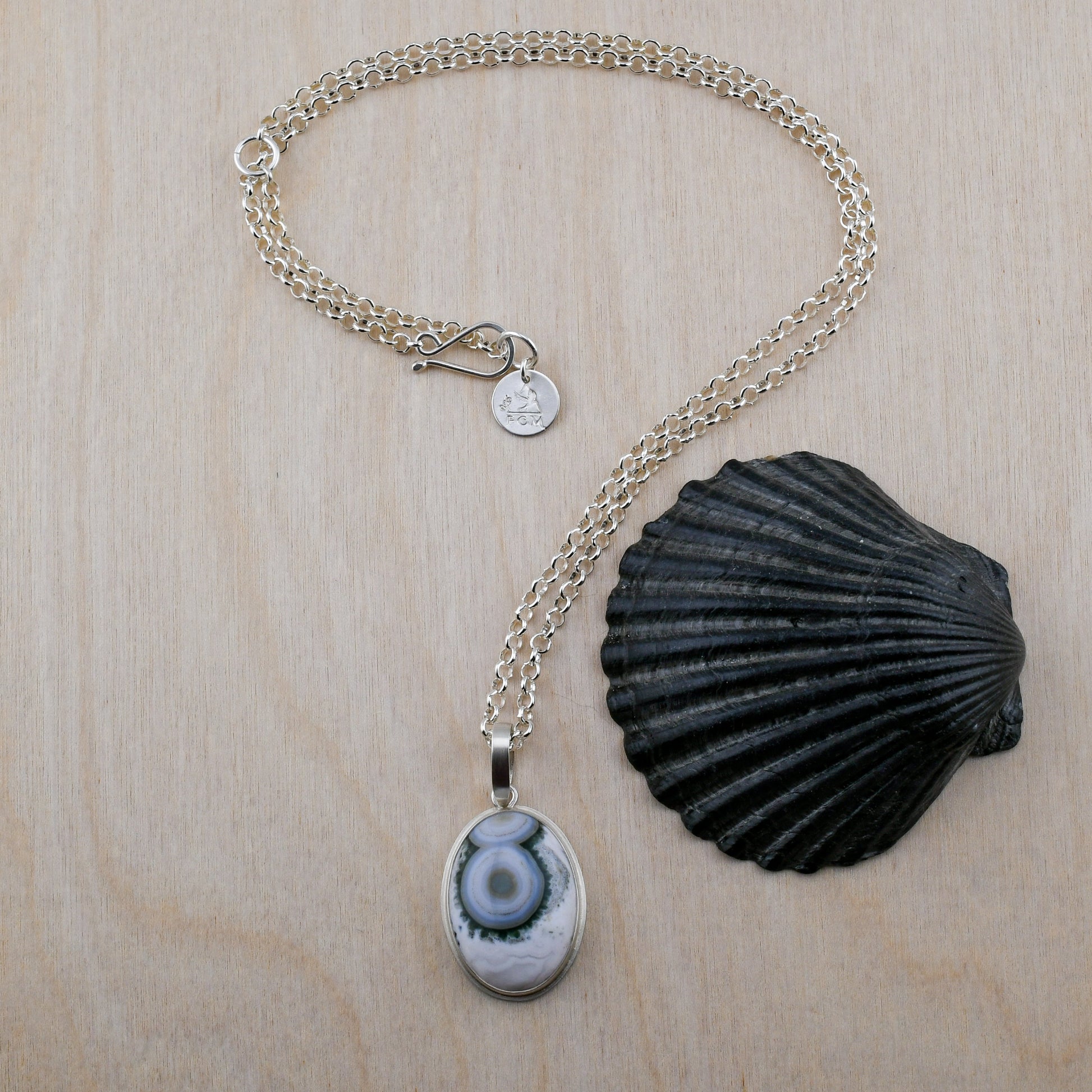 Necklace with a green and white ocean jasper pendant and shell on a wooden surface