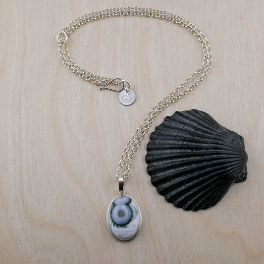 Necklace with a green and white ocean jasper pendant and shell on a wooden surface