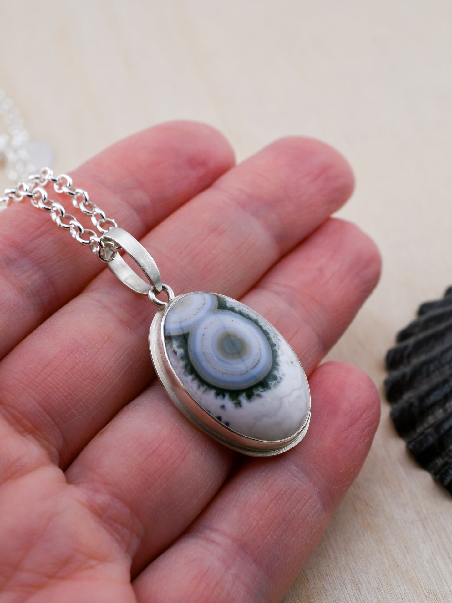 Necklace with a pendant featuring a green and white pattern held in a hand on a light background