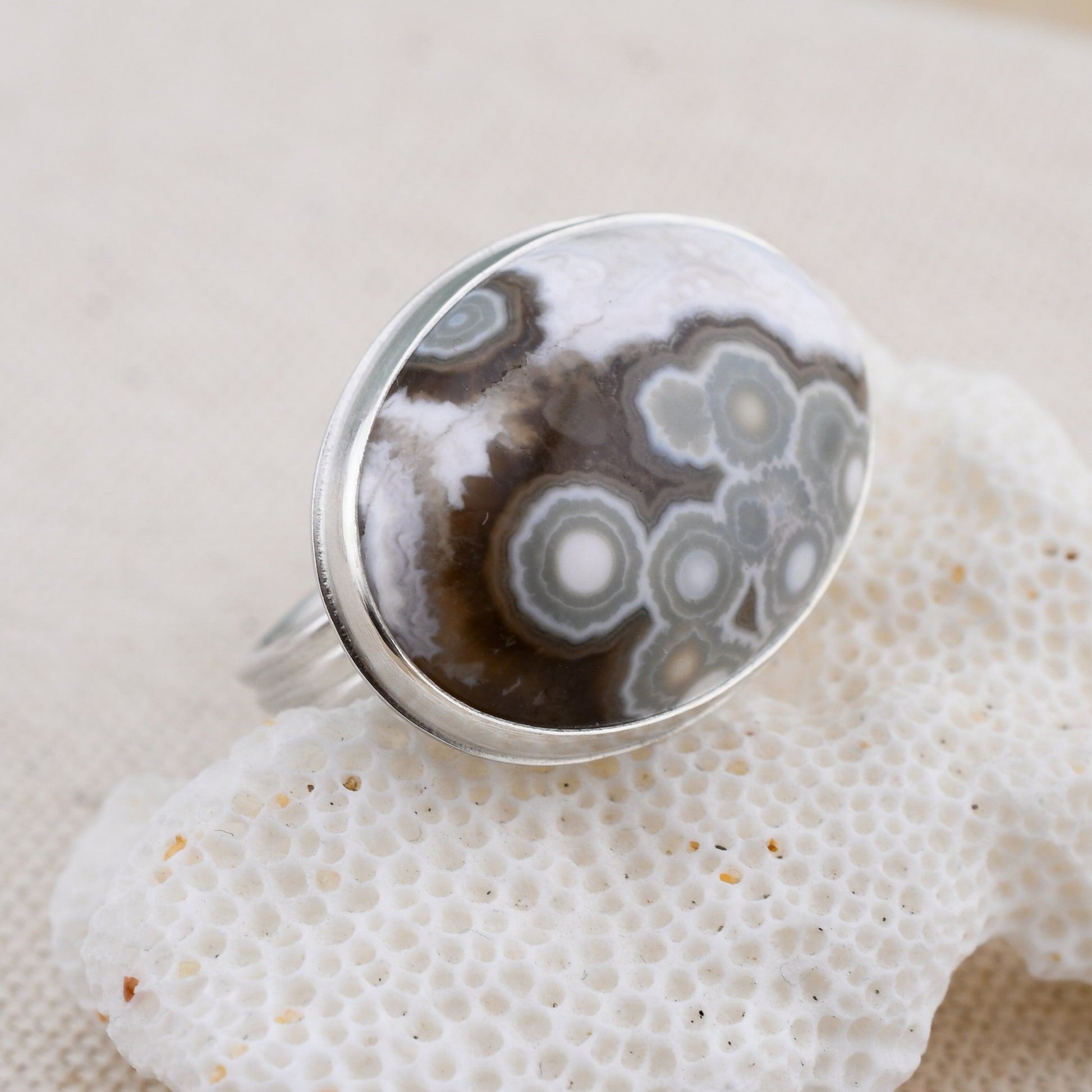 Silver ring with a brown and white ocean jasper on a textured white surface
