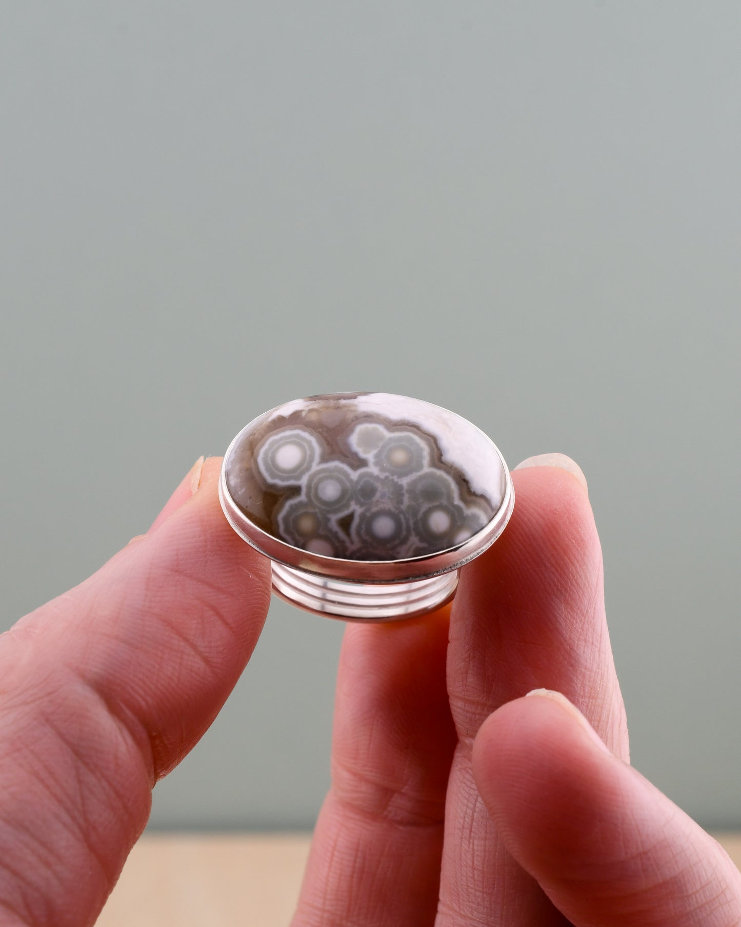 Hand holding a silver ring with jasper with concentric circle pattern against a plain background