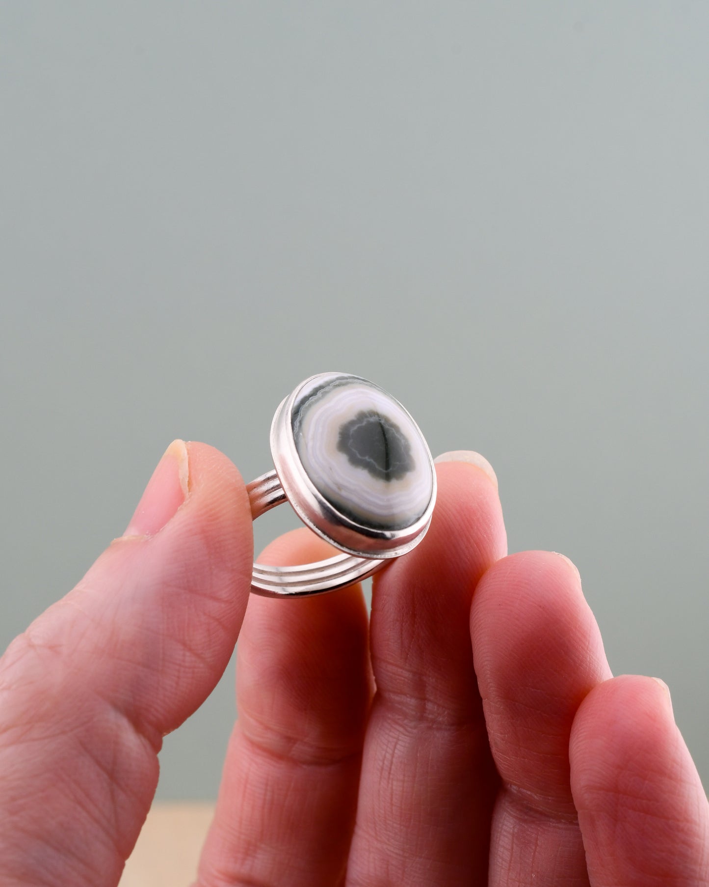 Silver ring with a green and white stone held between fingers against a gray background