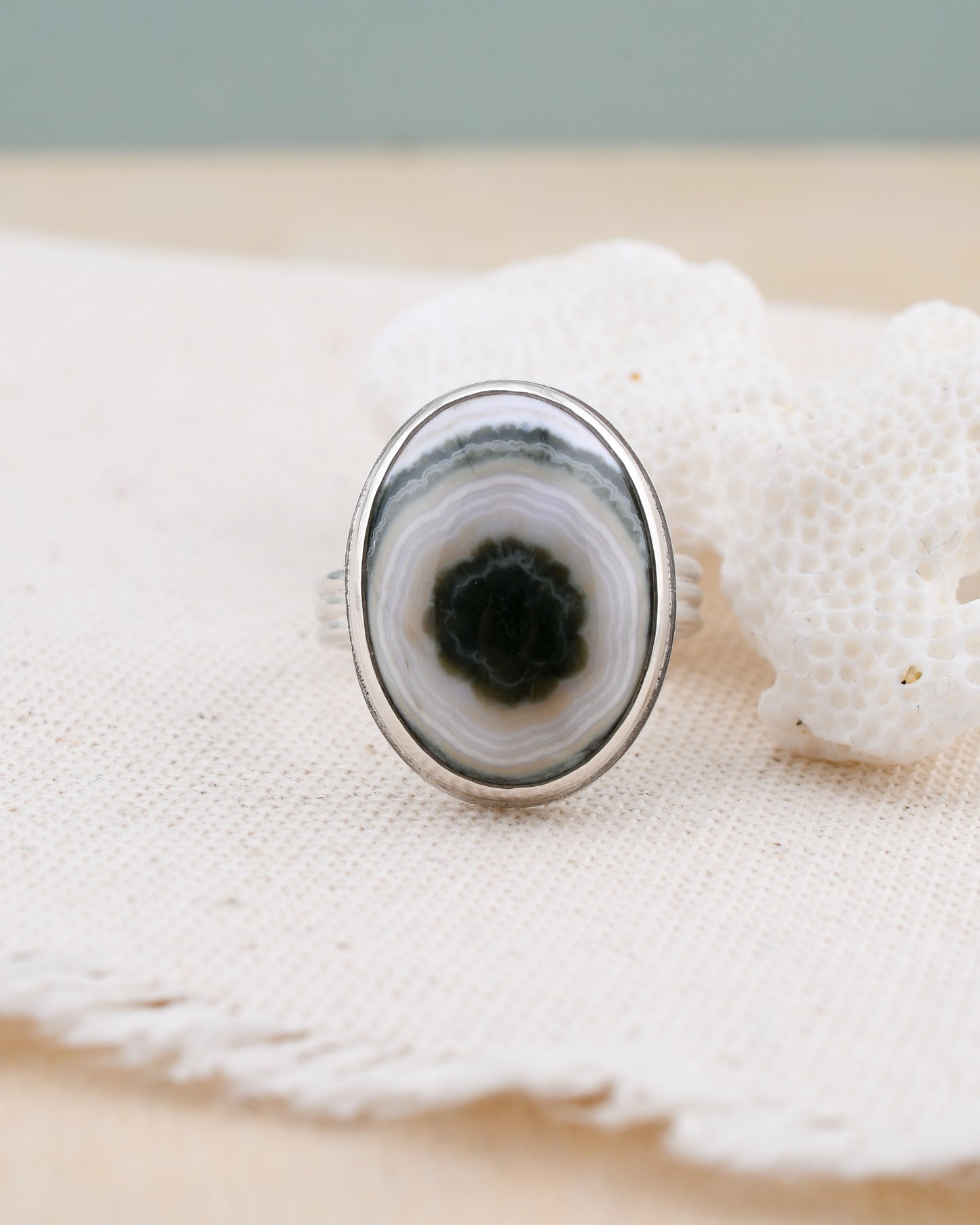 Close-up of a silver ring with a green and white jasper on a textured surface