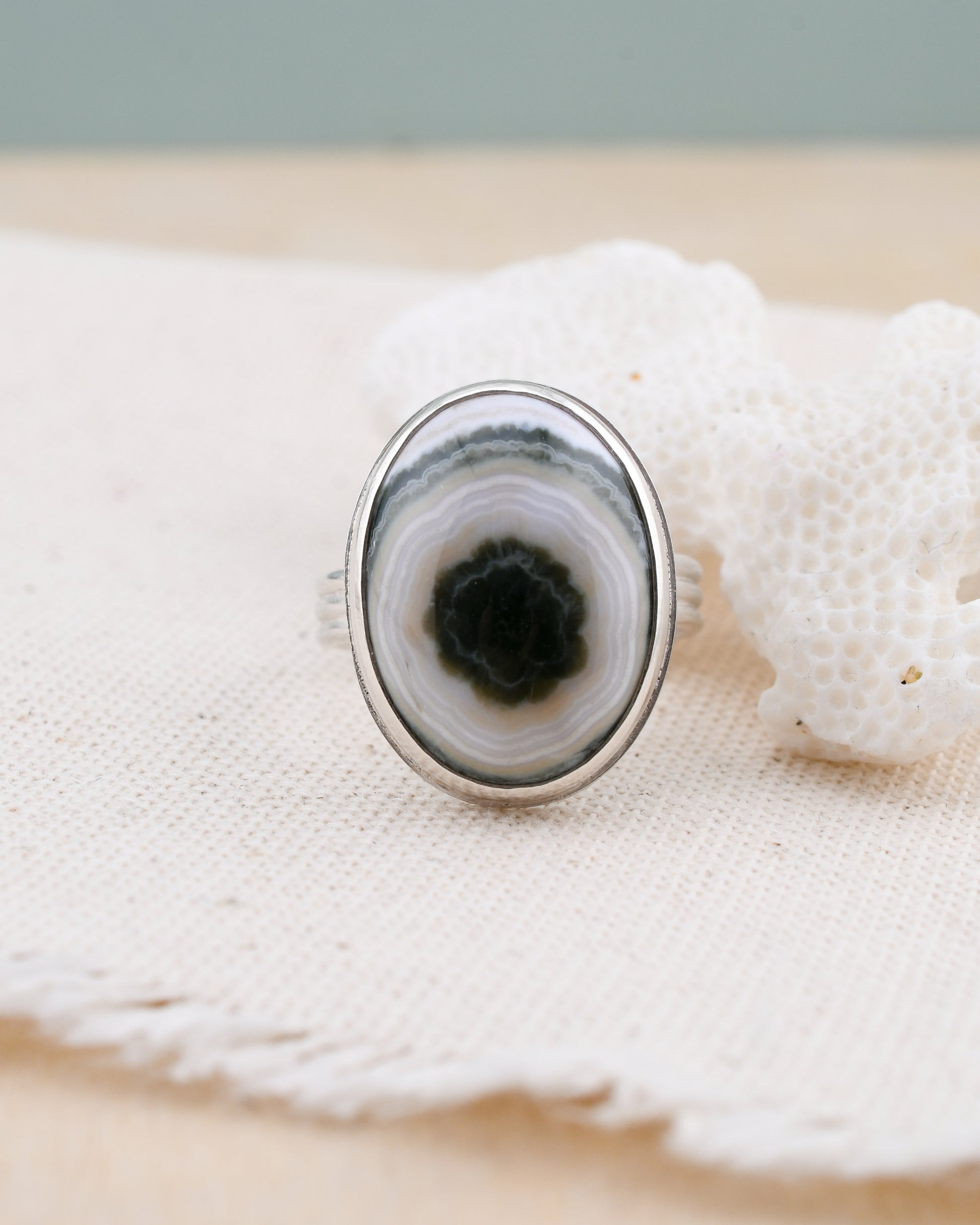 Close-up of a silver ring with a green and white jasper on a textured surface