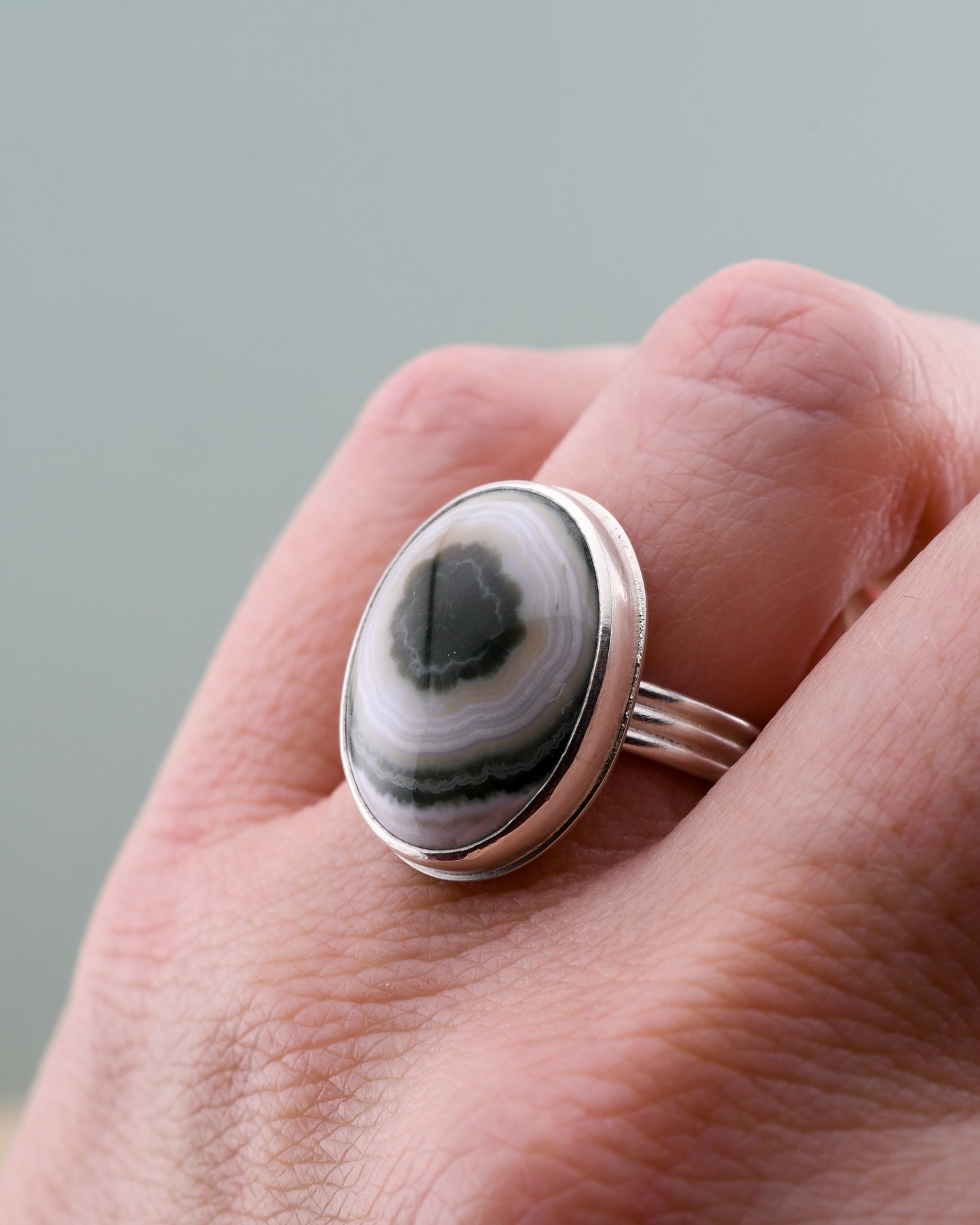 Silver ring with a green and white ocean jasper on a hand against a gray background
