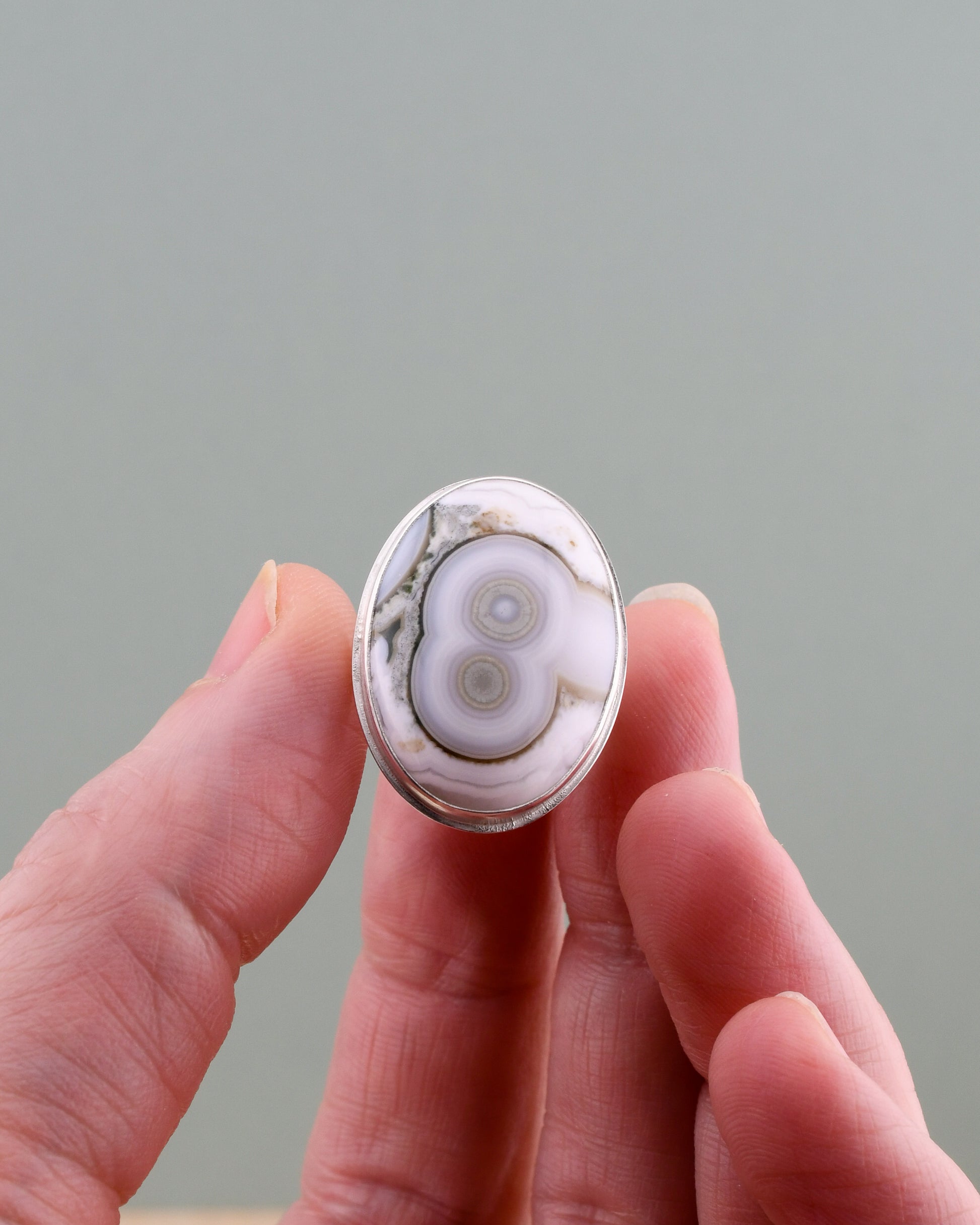 Hand holding an oval stone ring with intricate patterns against a plain background