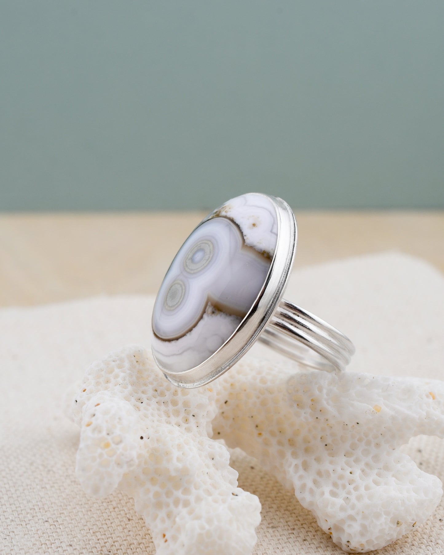 Silver ring with a white and green stone on a piece of coral against a gray background