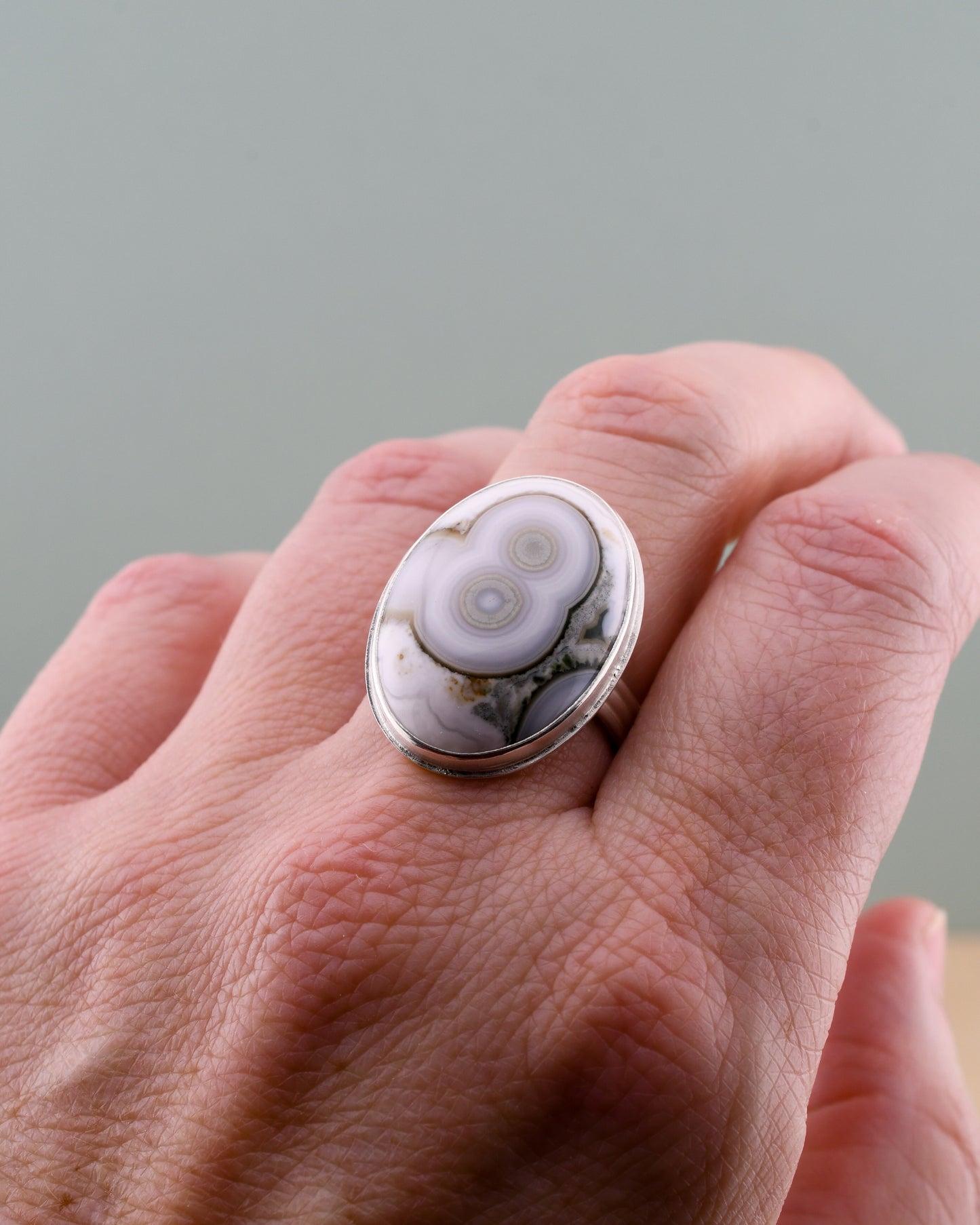 Hand wearing a ring with a large, oval-shaped stone on a neutral background