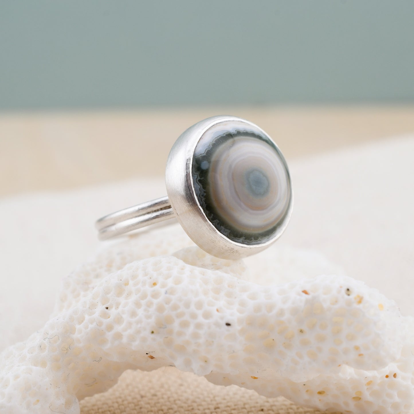 Silver ring with a round green and white stone on a piece of white coral