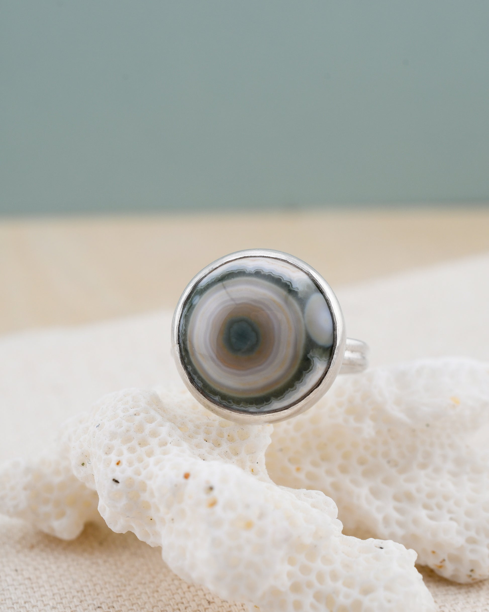 Silver ring with a round ocean jasper on a piece of white coral against a light gray background