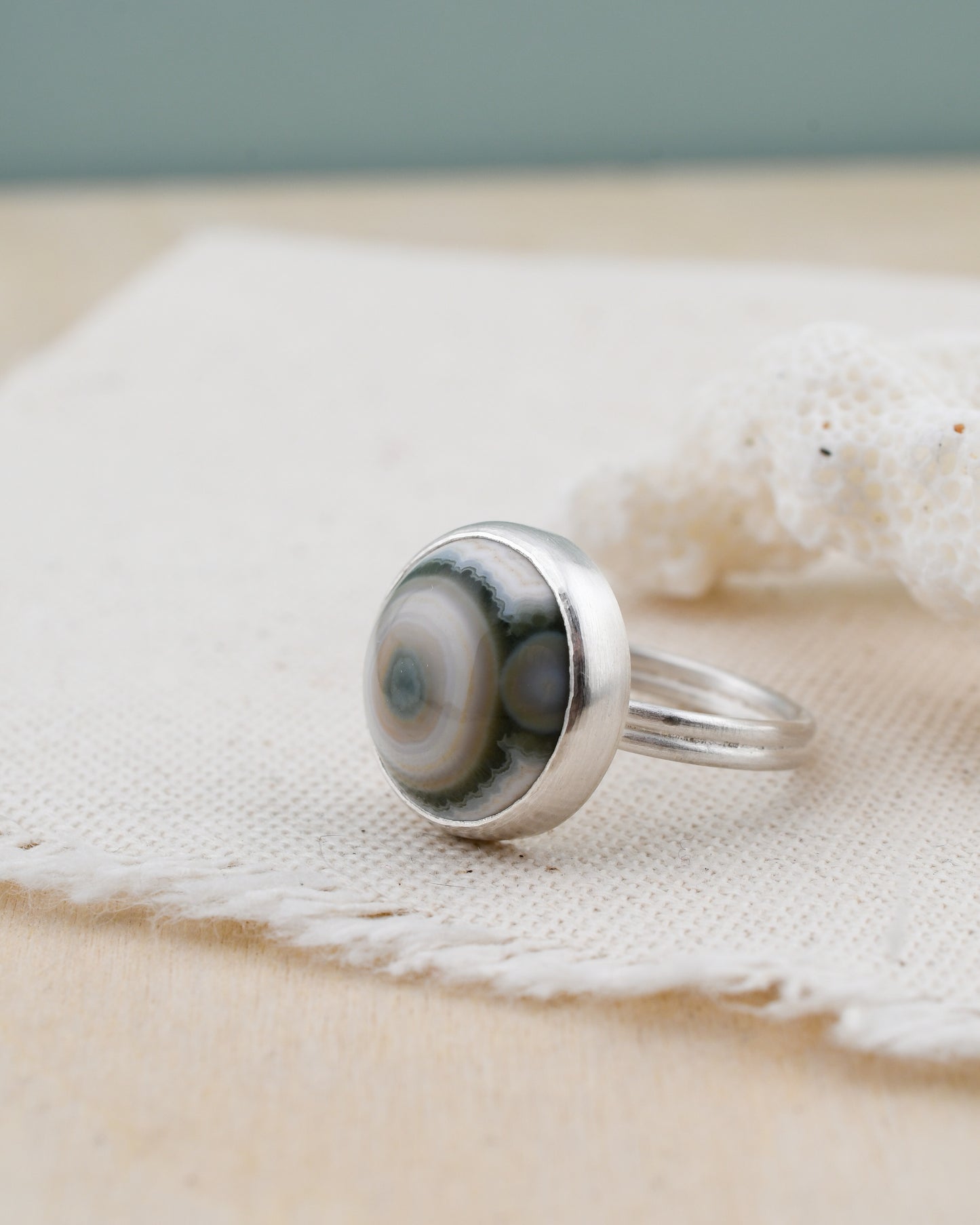 Silver ring with a round ocean jasper on a textured fabric background