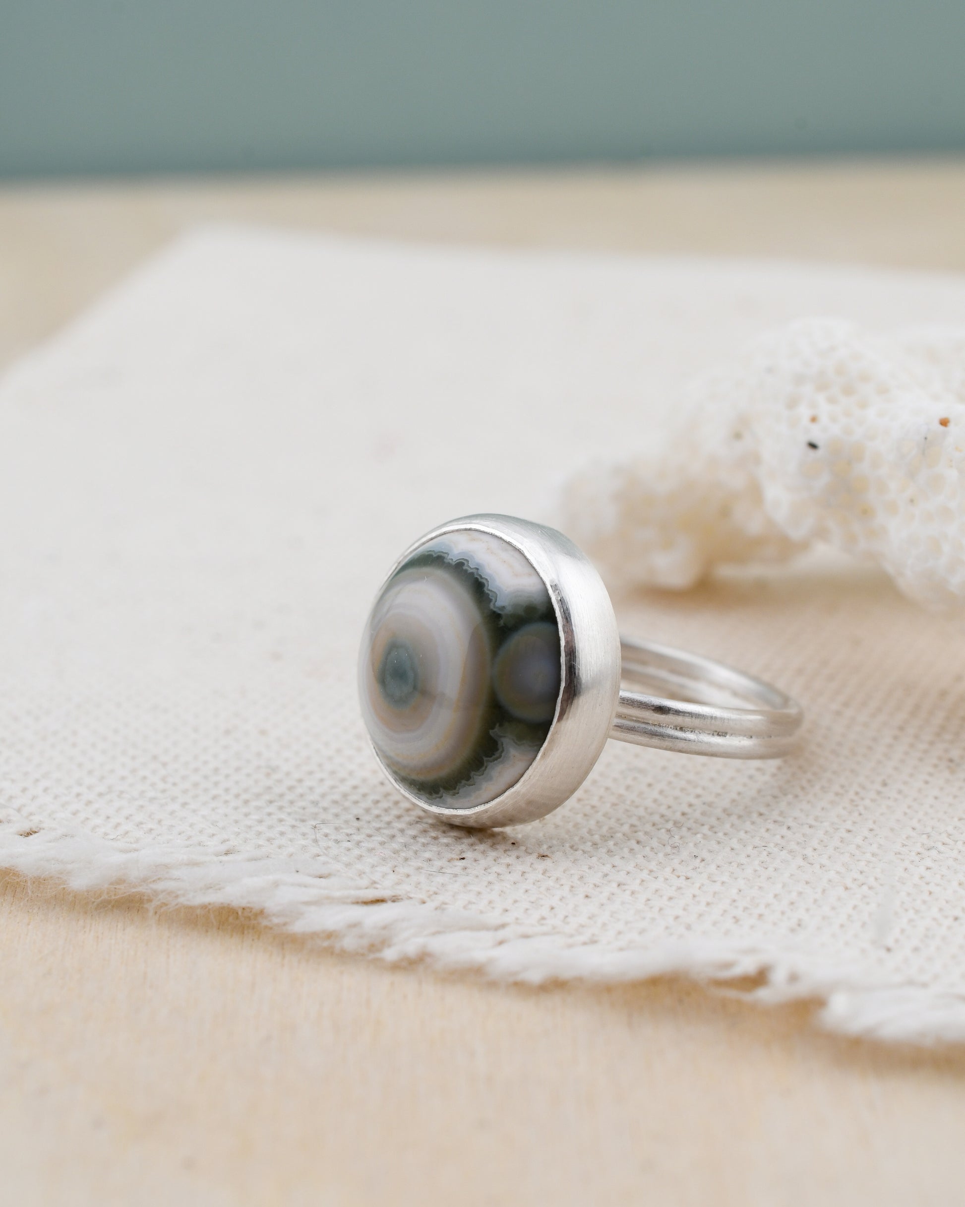 Silver ring with a round ocean jasper on a textured fabric background