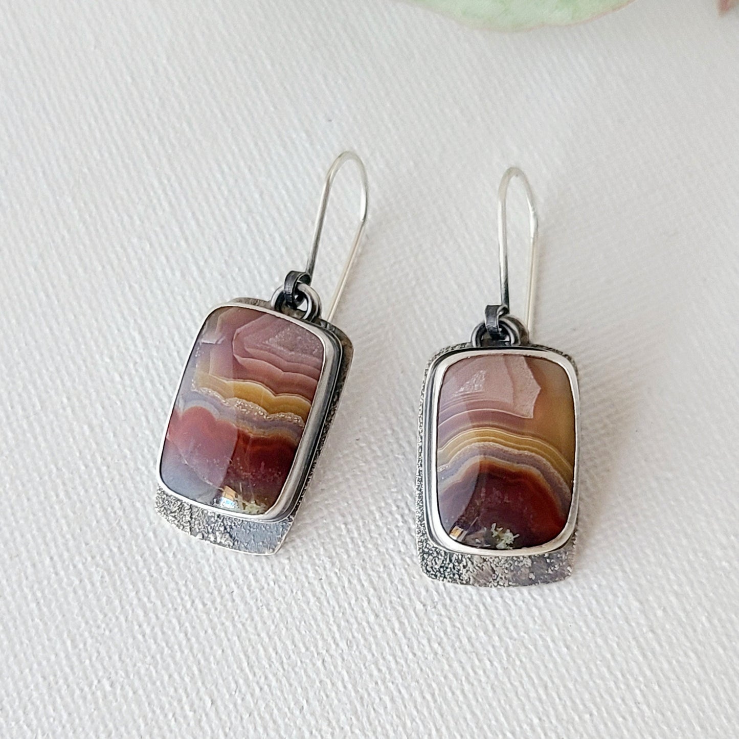 A pair of rectangular laguna lace agate earrings set in fine silver with a wavy striped pattern, showing deep red, periwinkle, and rose colors.