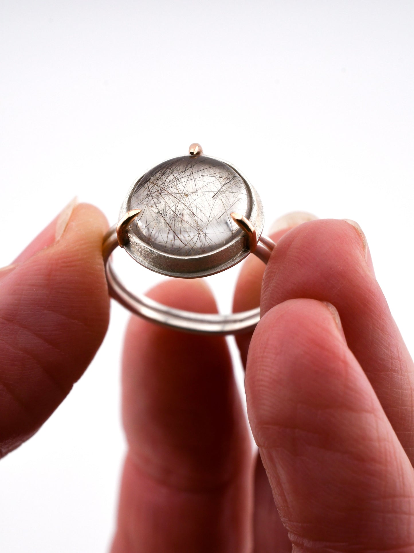 Hand holding a ring with a clear gemstone against a white background