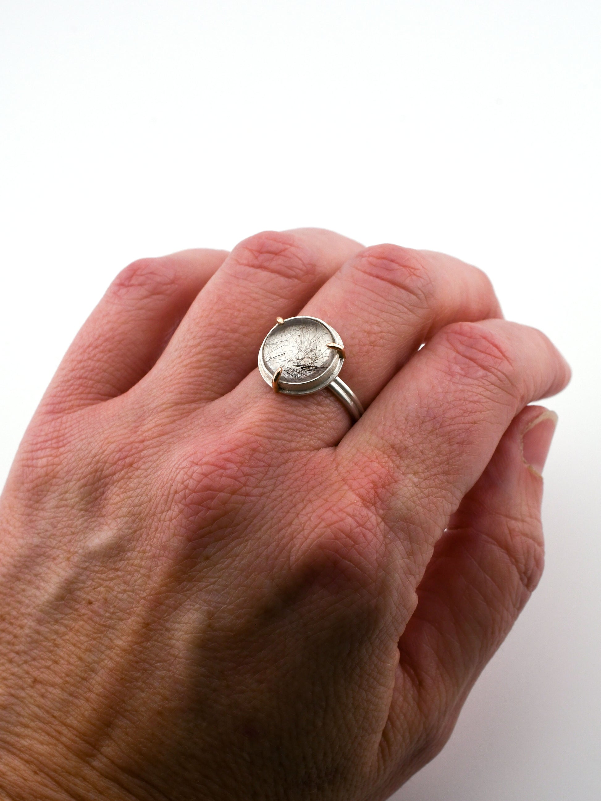 Hand wearing a silver ring with a circular design on a white background