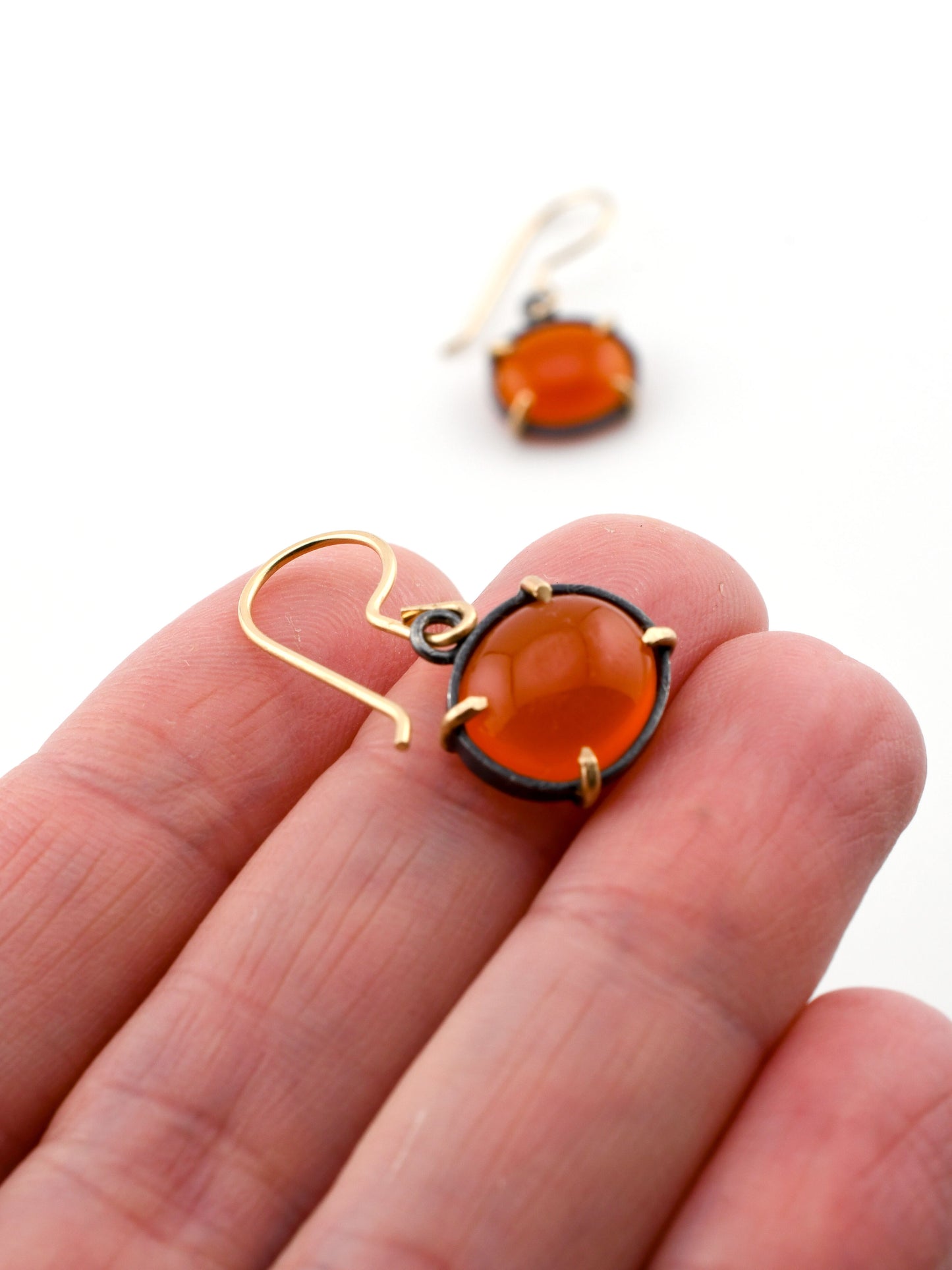 Close-up of a hand holding a gold and black earring with an orange gemstone.
