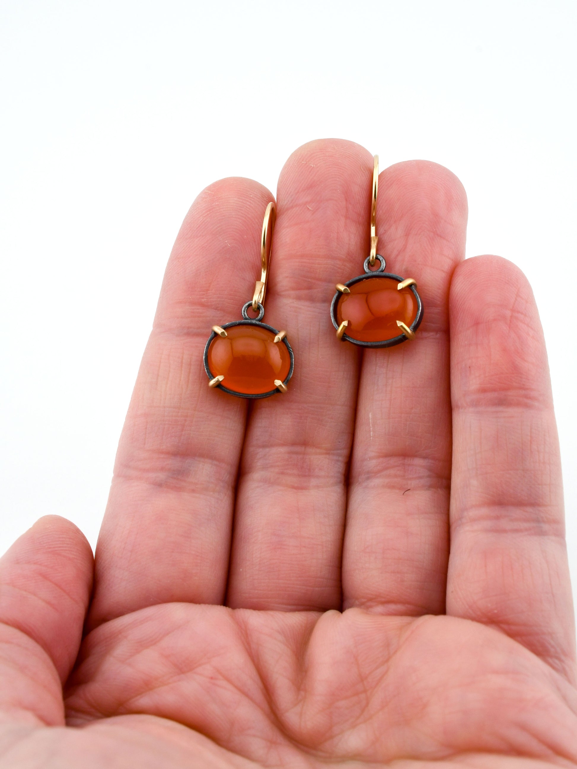 Gold earrings with orange gemstones held in a hand on a white background