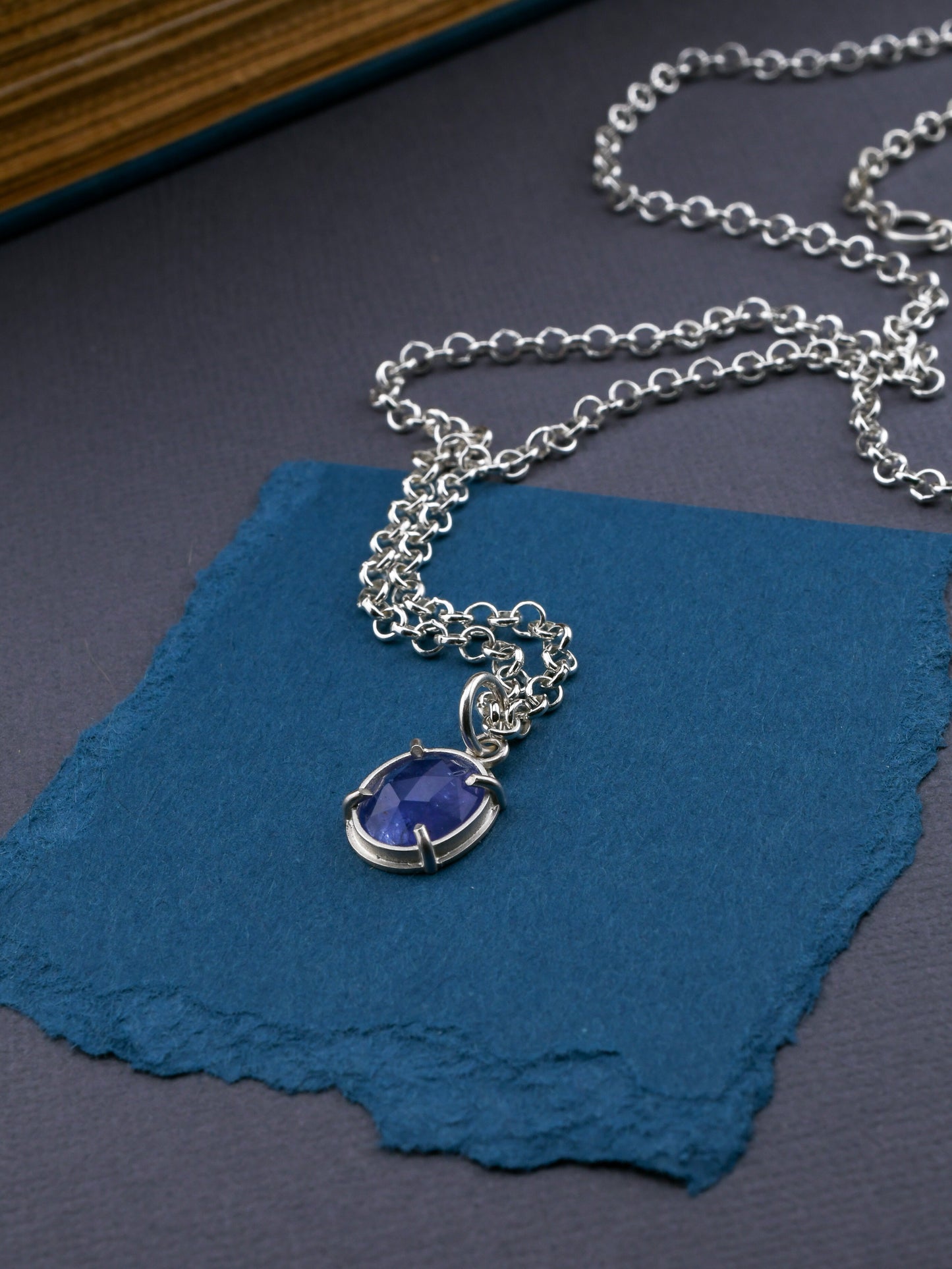 Silver necklace with a blue pendant on a blue textured surface