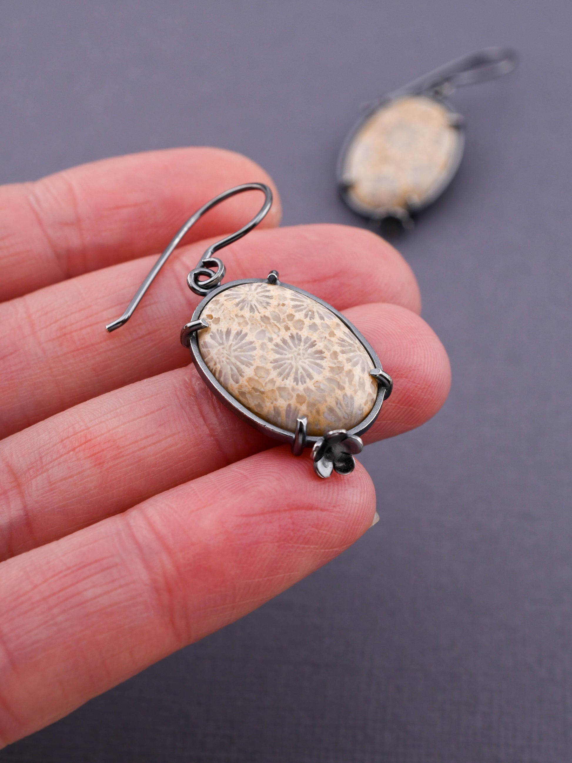 Fossilized coral earring held between fingers against a dark background