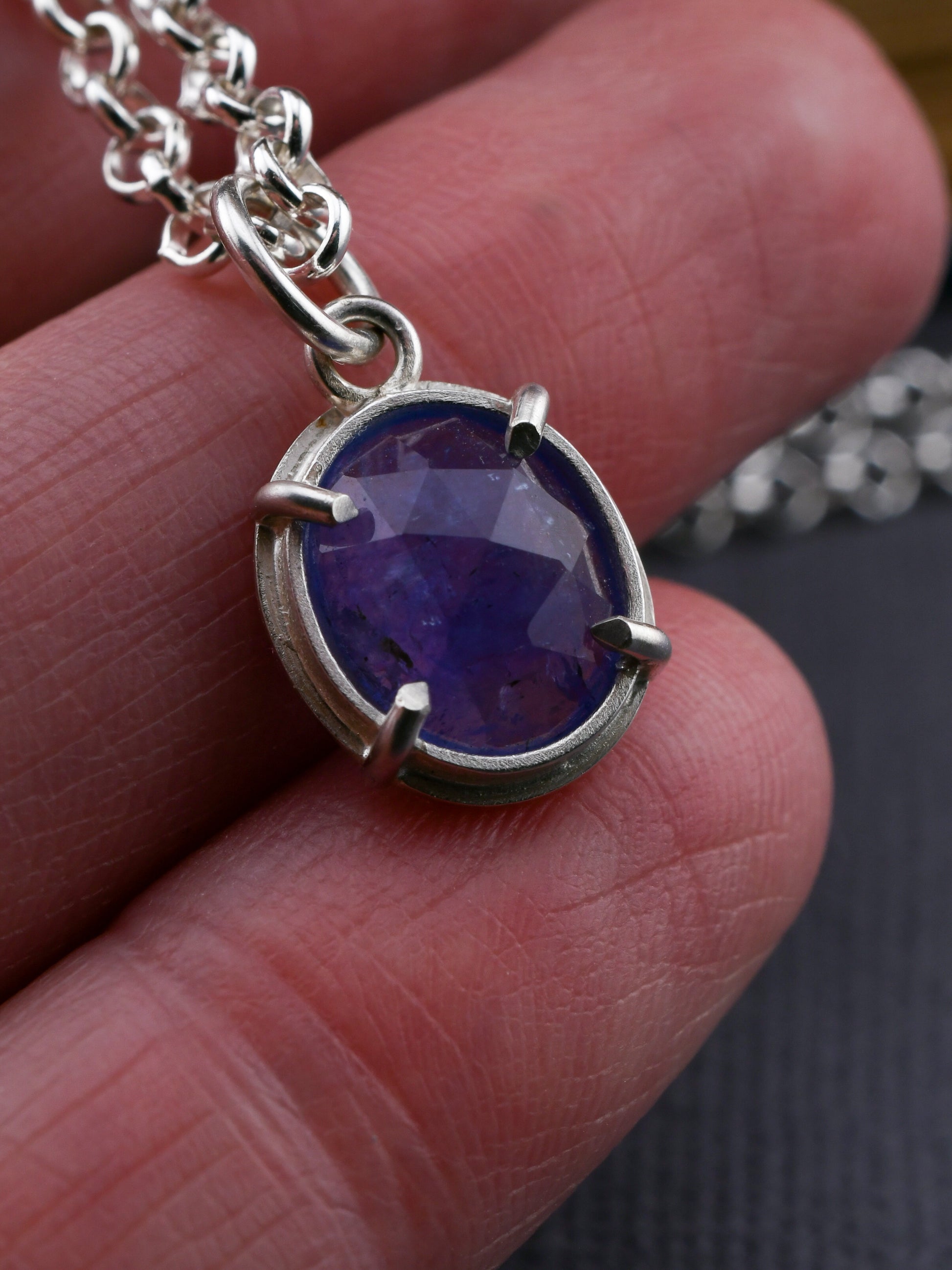 Silver necklace with a purple gemstone pendant held between fingers.