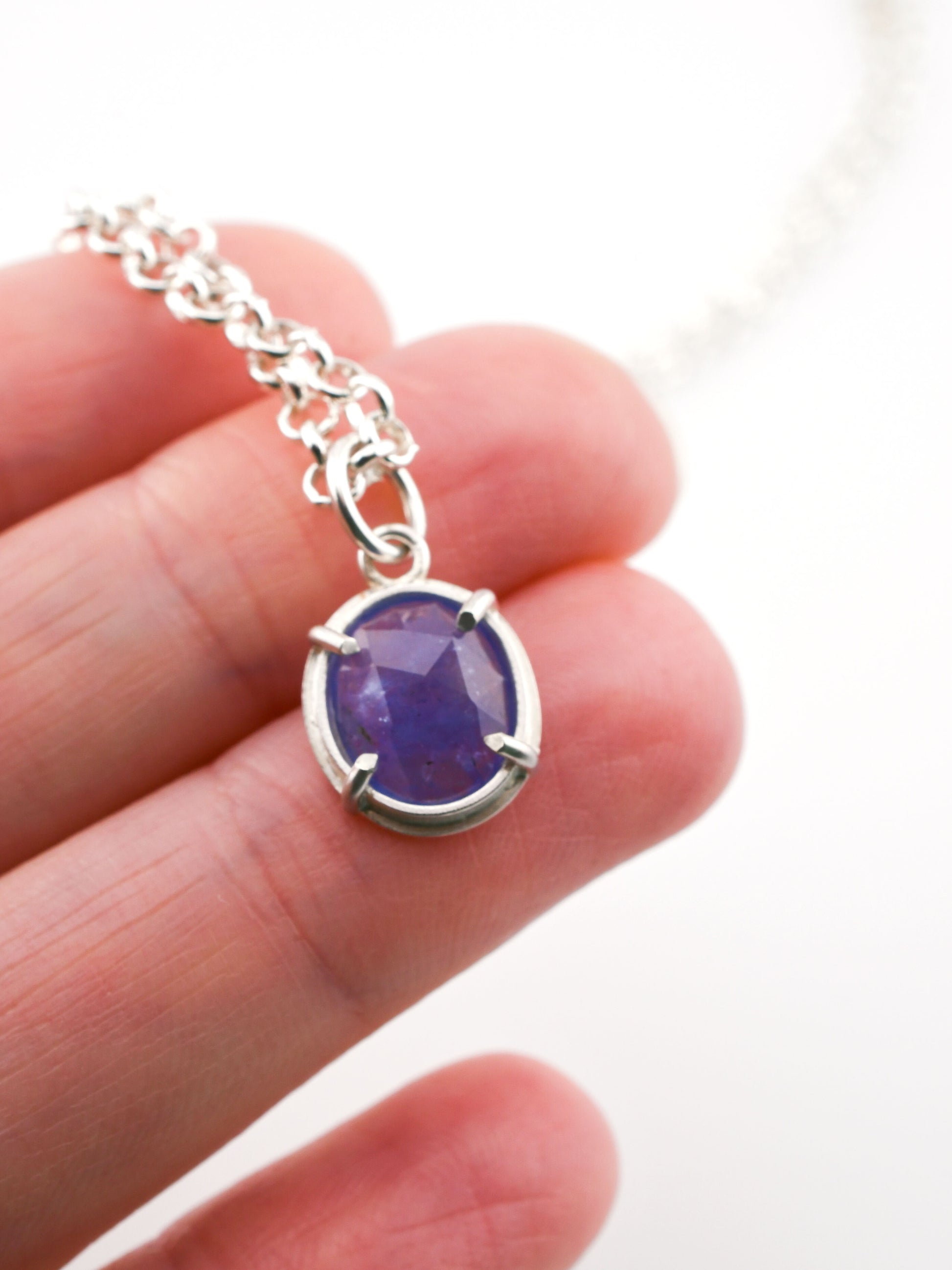 Silver necklace with a purple gemstone held between fingers on a white background